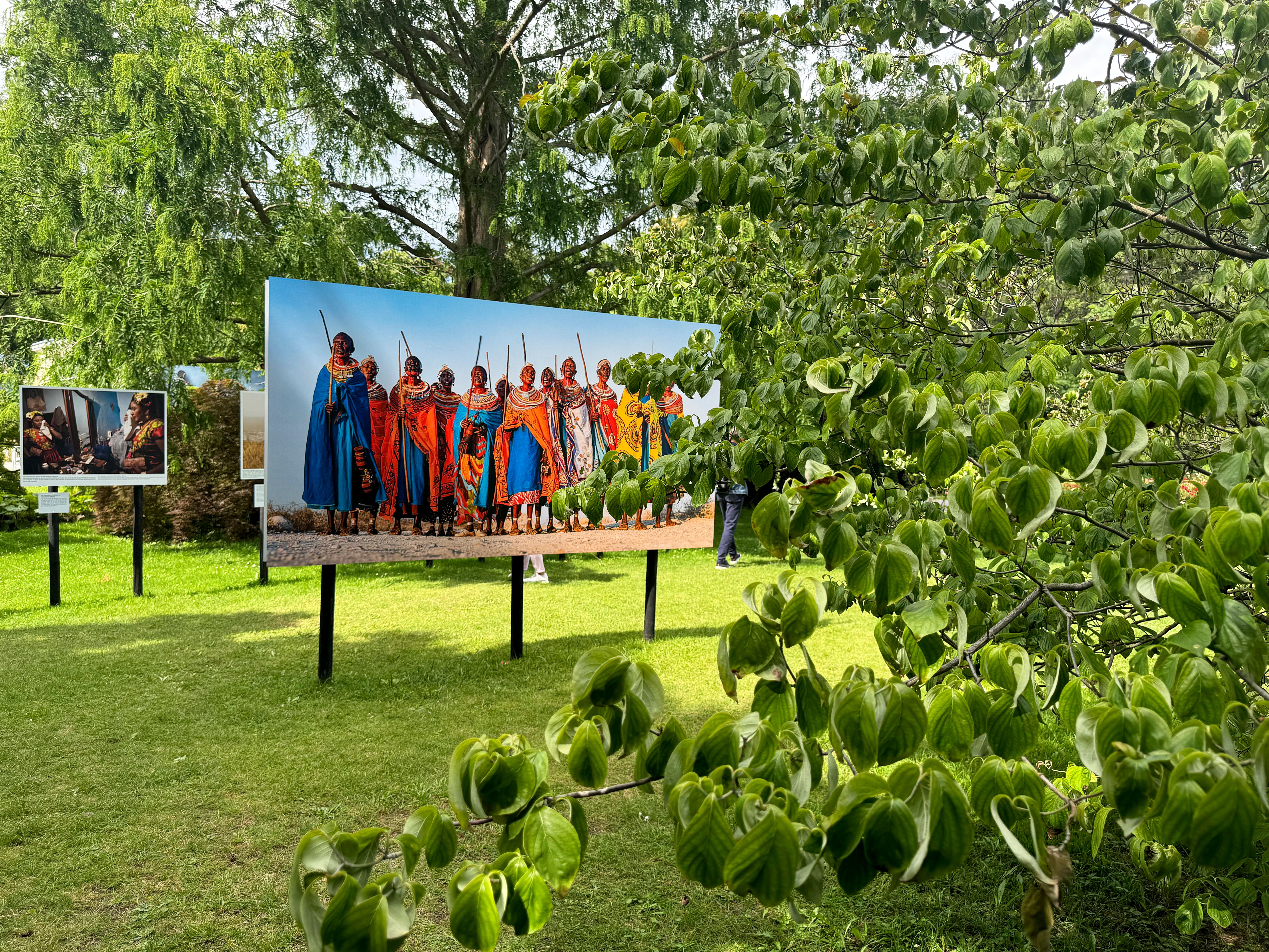 Outdoor-Fotoausstellung mit Bildern von Menschen in traditioneller Kleidung auf einer Wiese.