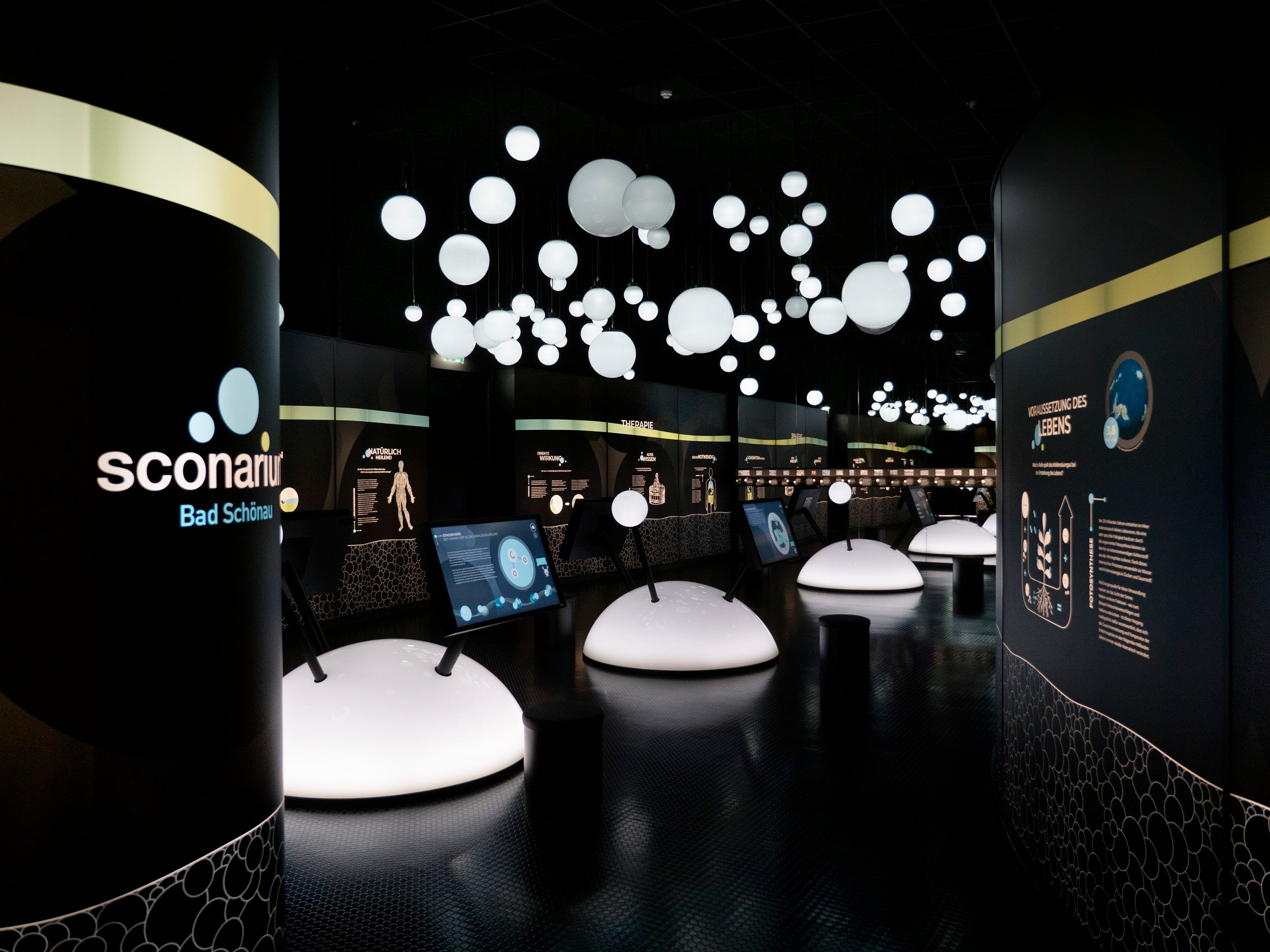 Innenansicht einer modernen Ausstellung mit beleuchteten Kugeln und interaktiven Displays.