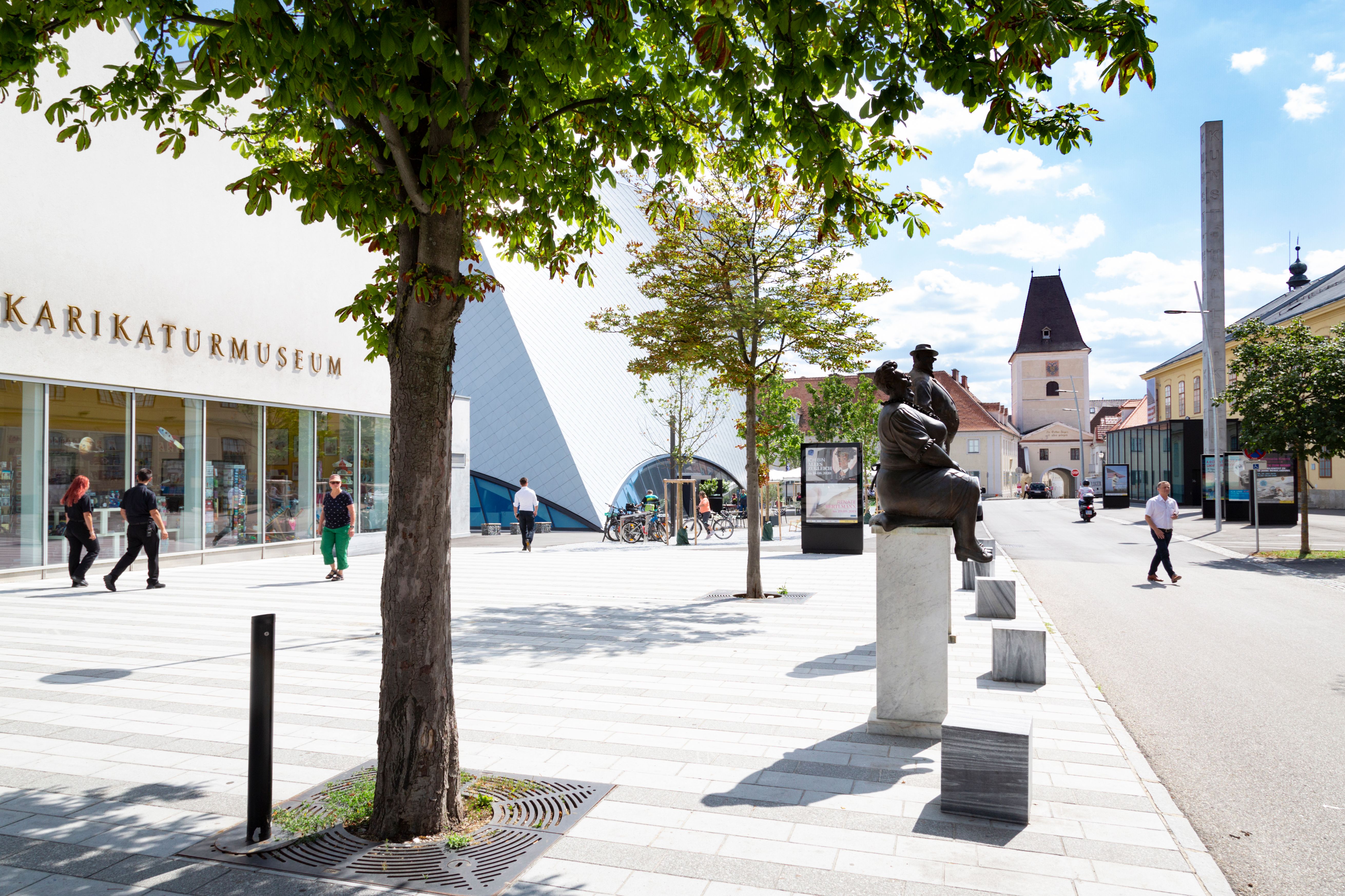 Außenansicht des Karikaturmuseums Krems mit Statuen und Bäumen.