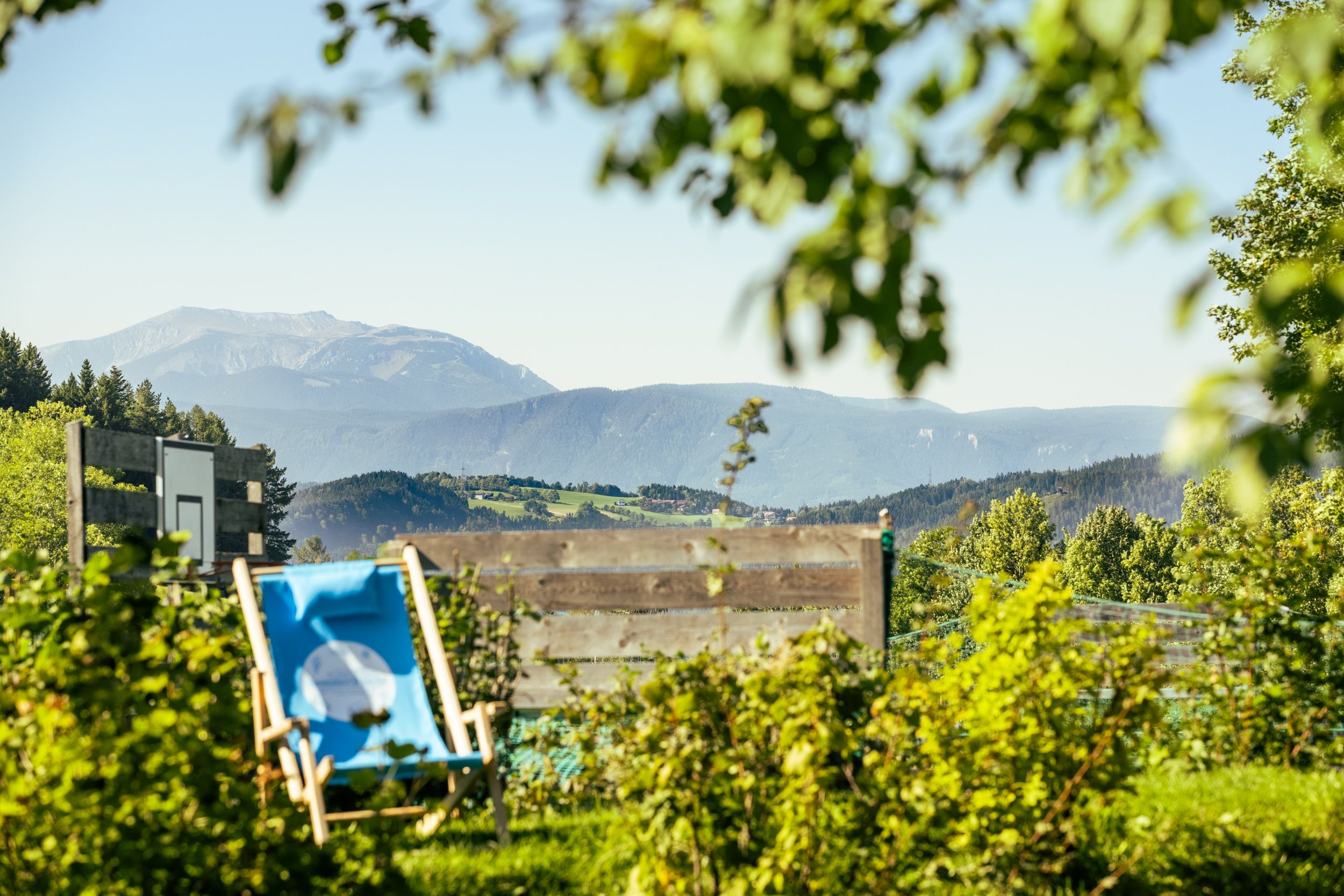 Blick von einem Garten auf eine Berglandschaft mit Liegestuhl im Vordergrund.
