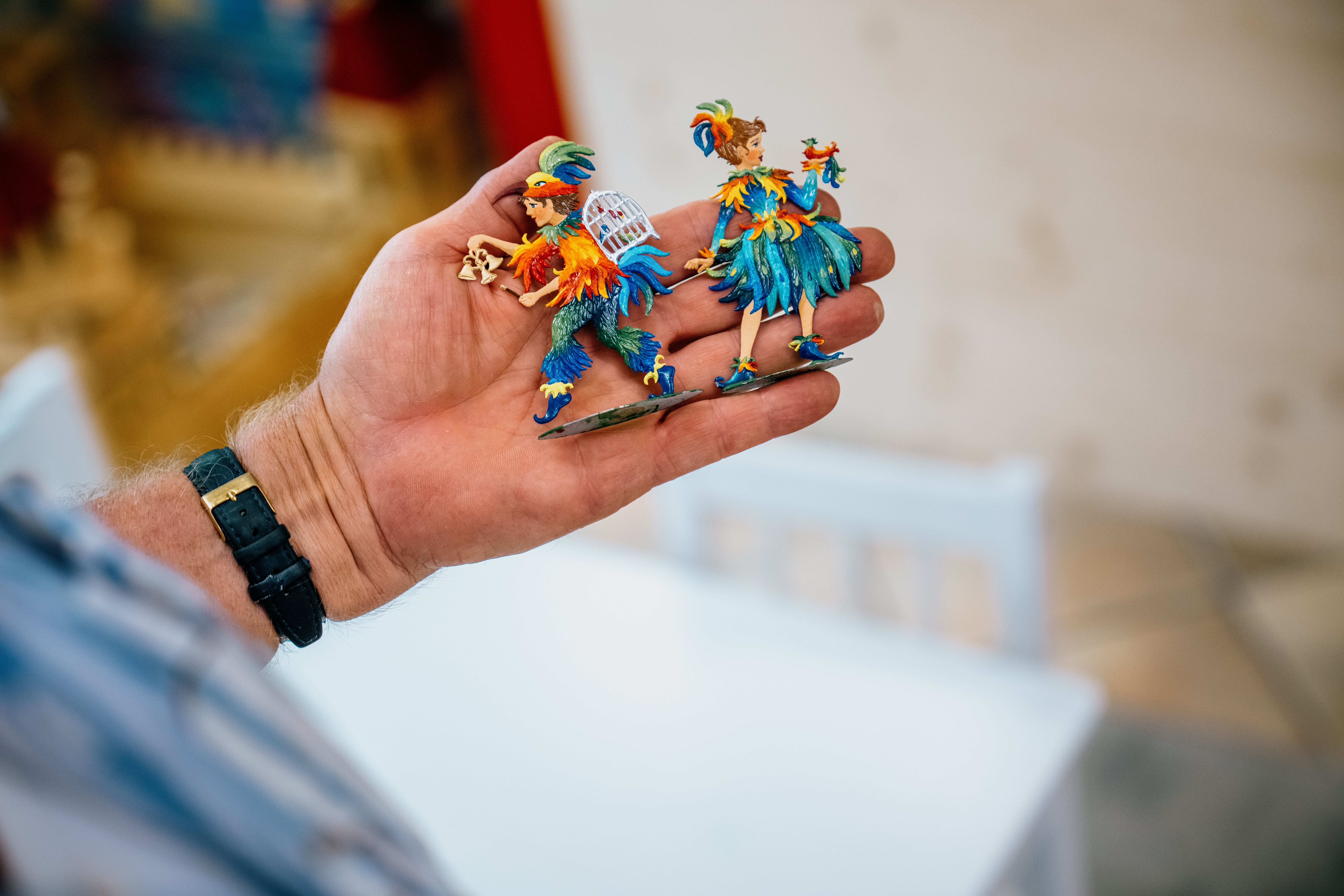 Eine Hand hält zwei bunte Zinnfiguren in Papageienkostümen.