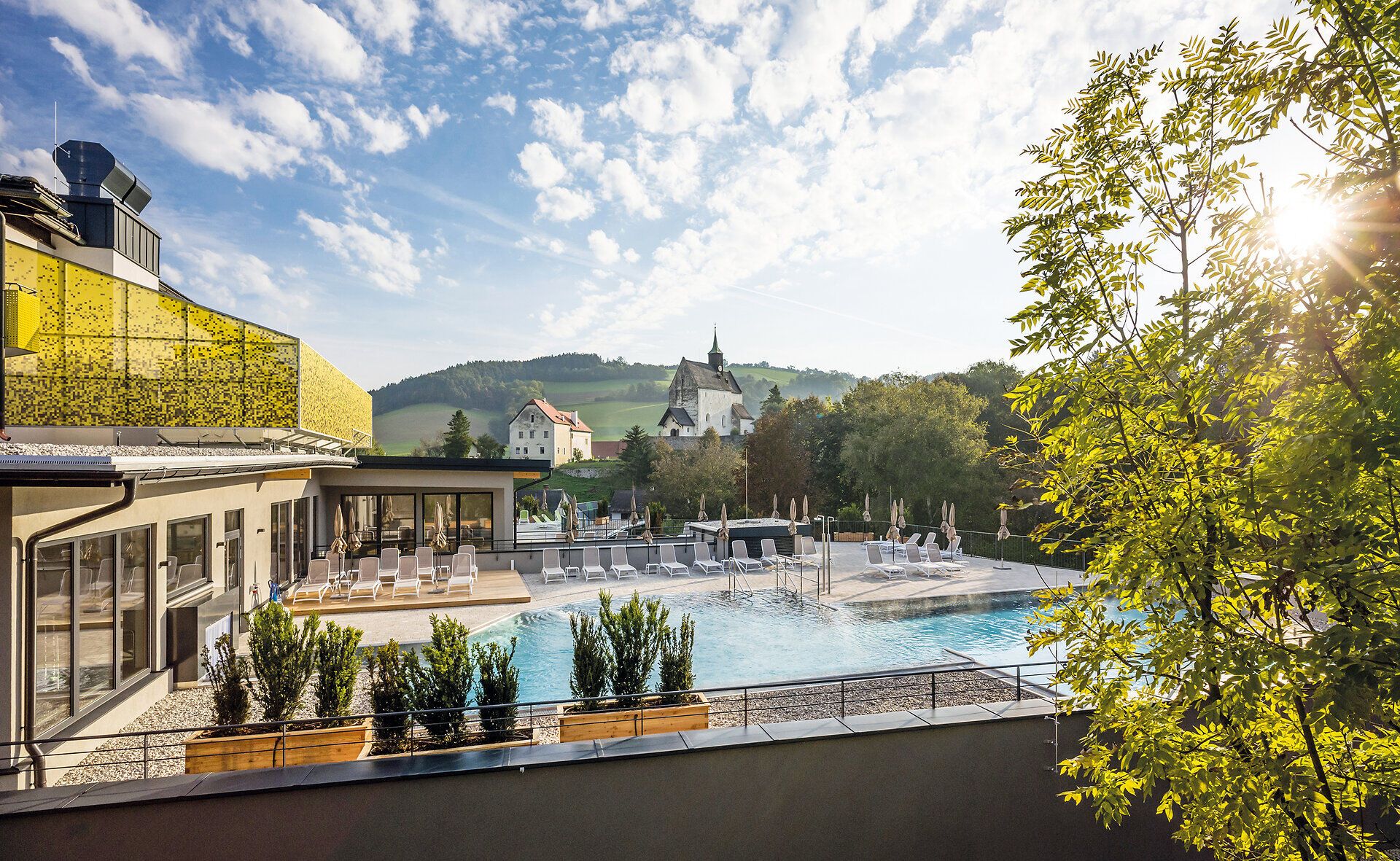Einladend strahlt der Außenpool des Resorts in der warmen Sonne, umgeben von üppigem Grün und sanften Hügeln. Die ruhige Atmosphäre lädt dazu ein, die Seele baumeln zu lassen und die Schönheit der Natur zu genießen.