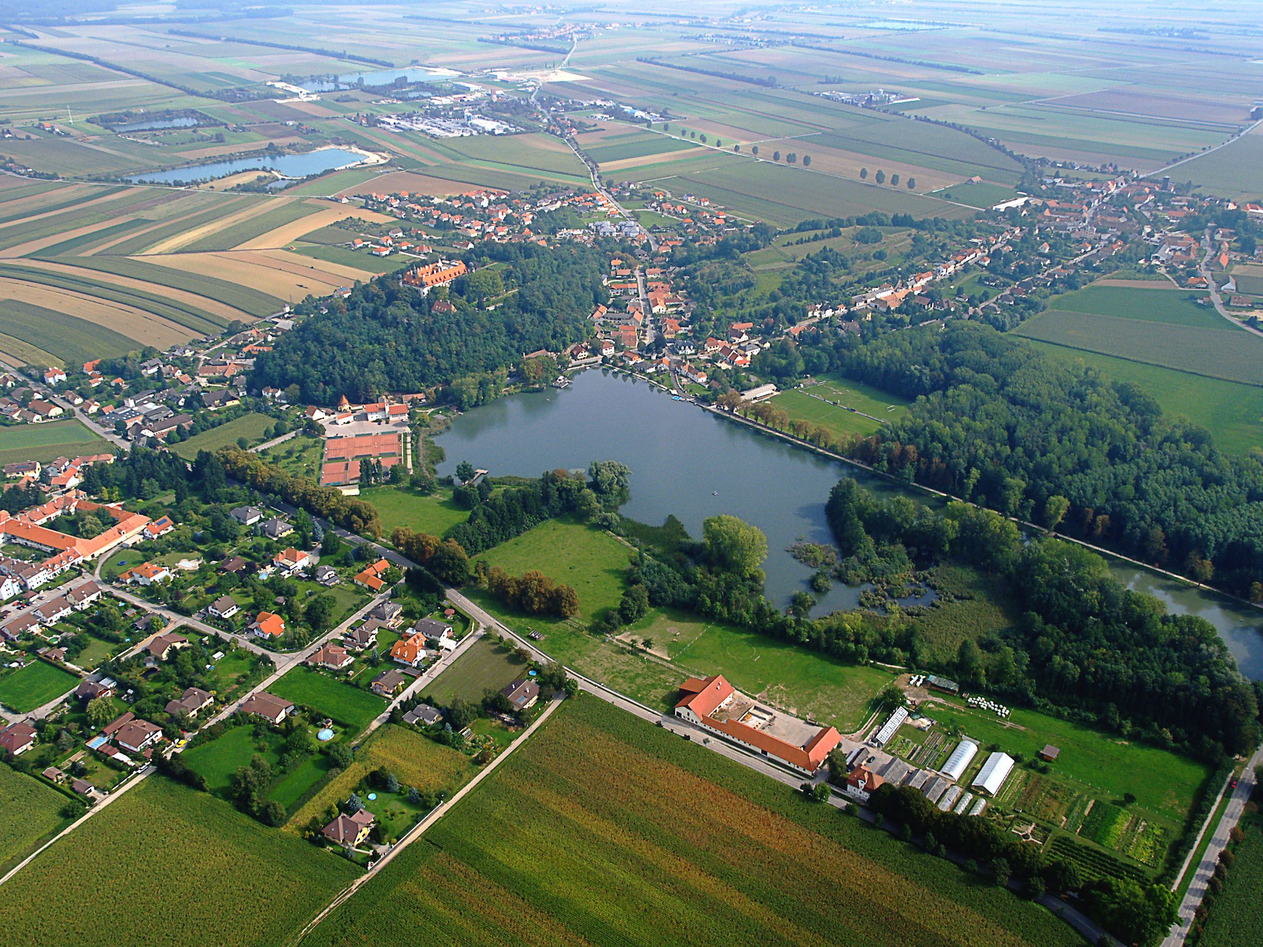 Luftaufnahme von Sitzenberg-Reidling mit Schloss, See und umliegenden Feldern.