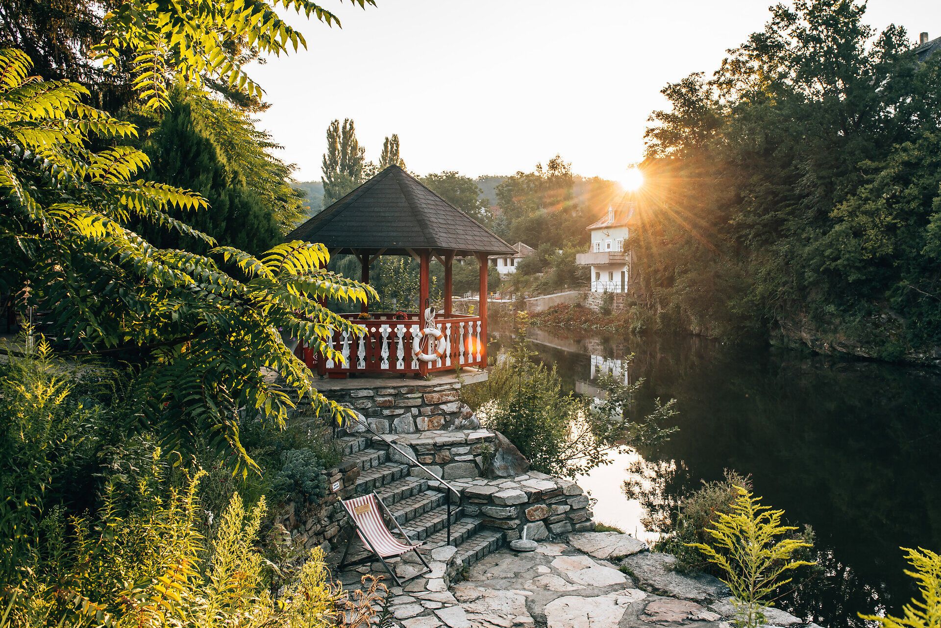 Ruhiges Ufer am Kamp im Strandbad Plank am Kamp mit Pavillon über dem Wasser und einem Liegestuhl am Ufer des Flusses. 