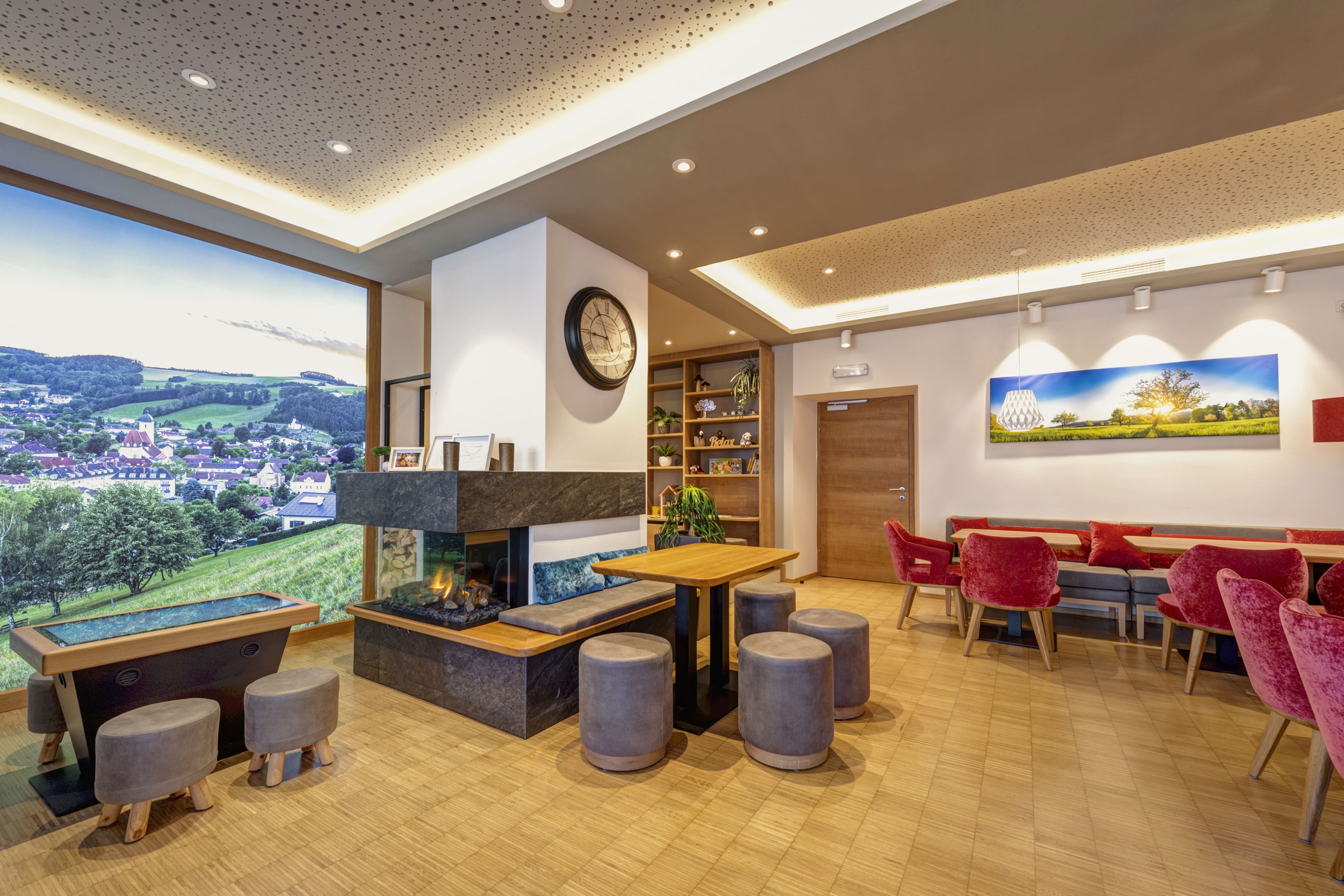 Innenansicht eines modernen Bistros mit Kamin, roten Stühlen und großem Landschaftsbild an der Wand.