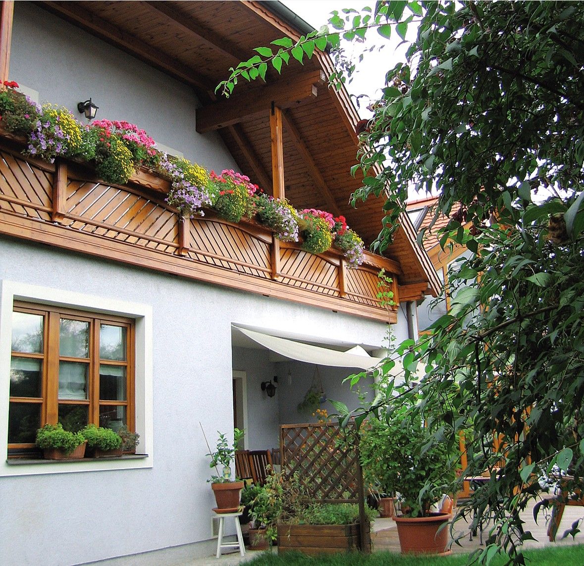 Ein Gästehaus mit Holzbalkon und blühenden Blumen, umgeben von grünen Pflanzen.