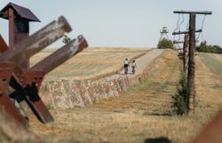 Zwei Radfahrer auf einem Weg neben einem alten Grenzzaun und einem Wachturm.