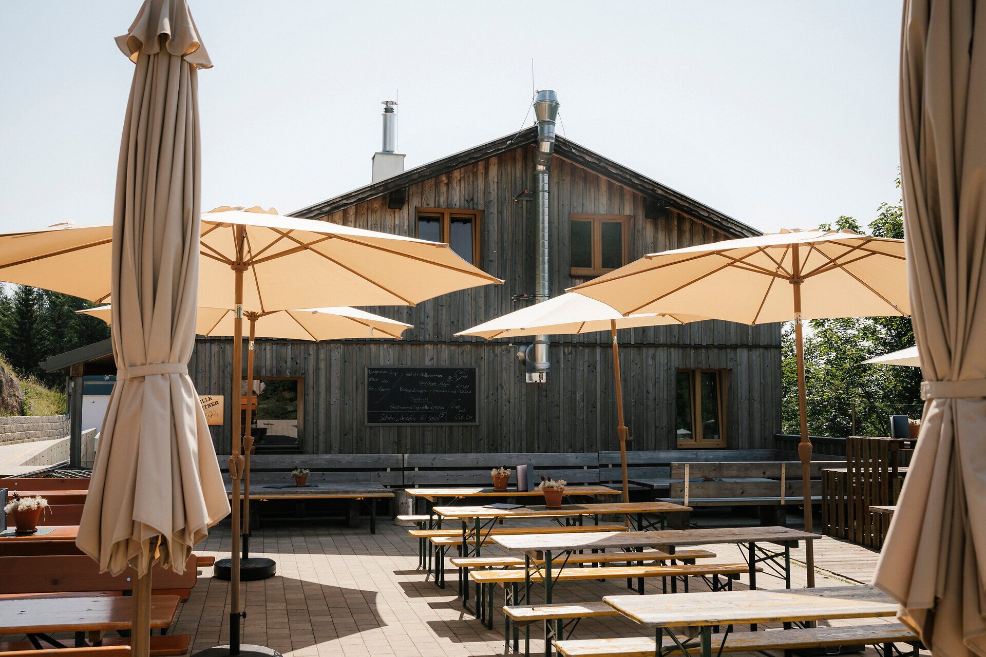Terrasse der Schutzhütte Haltestelle Baumgartner mit Sitzbänken und großen Sonnenschirmen