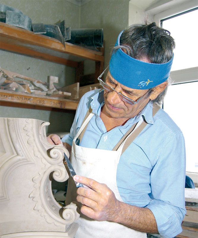 Ein Restaurator arbeitet an einem dekorativen Element mit einem Werkzeug.