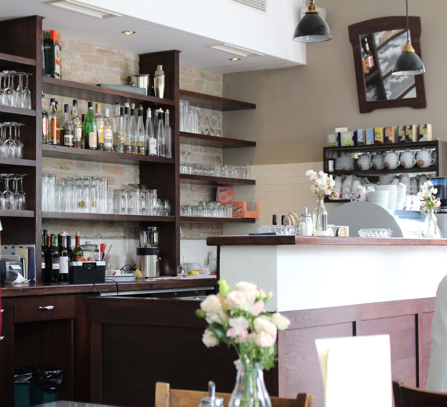 Innenansicht einer Bar mit Regalen voller Gläser und Flaschen, Blumen auf dem Tresen.