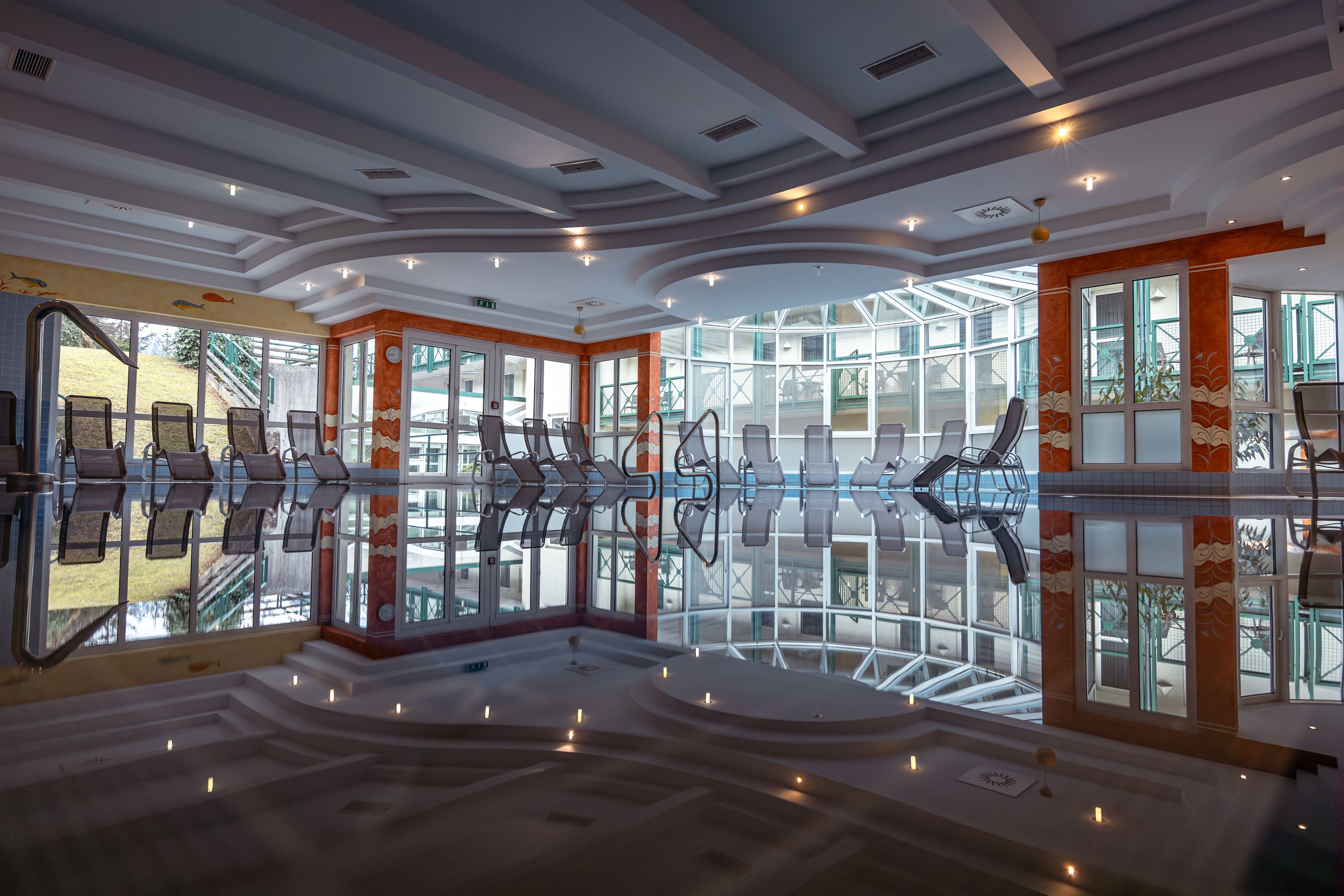 Innenansicht eines Hotelpools mit Liegestühlen und Glasfront.