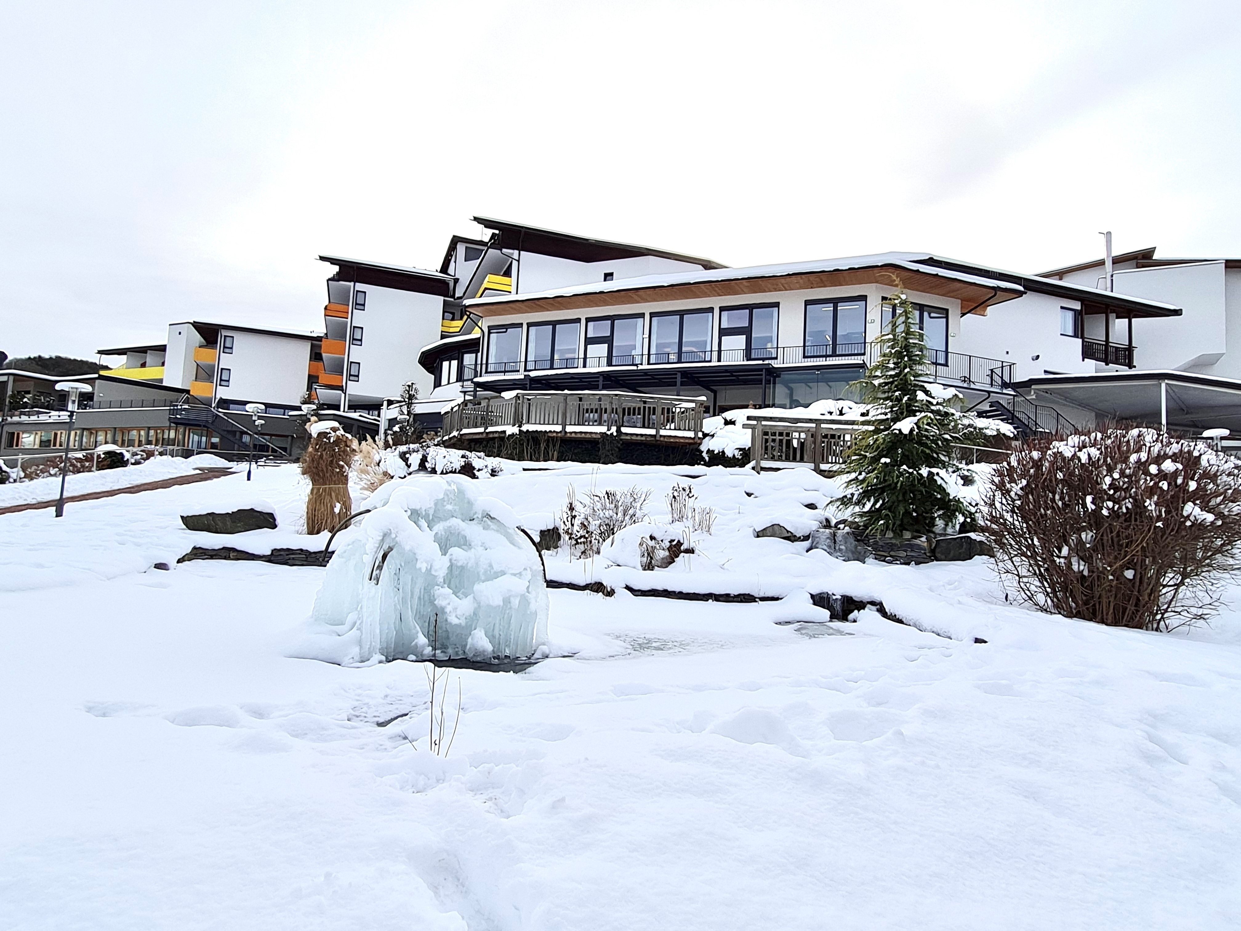 Verschneites Hotelgebäude mit gefrorenem Brunnen im Vordergrund.