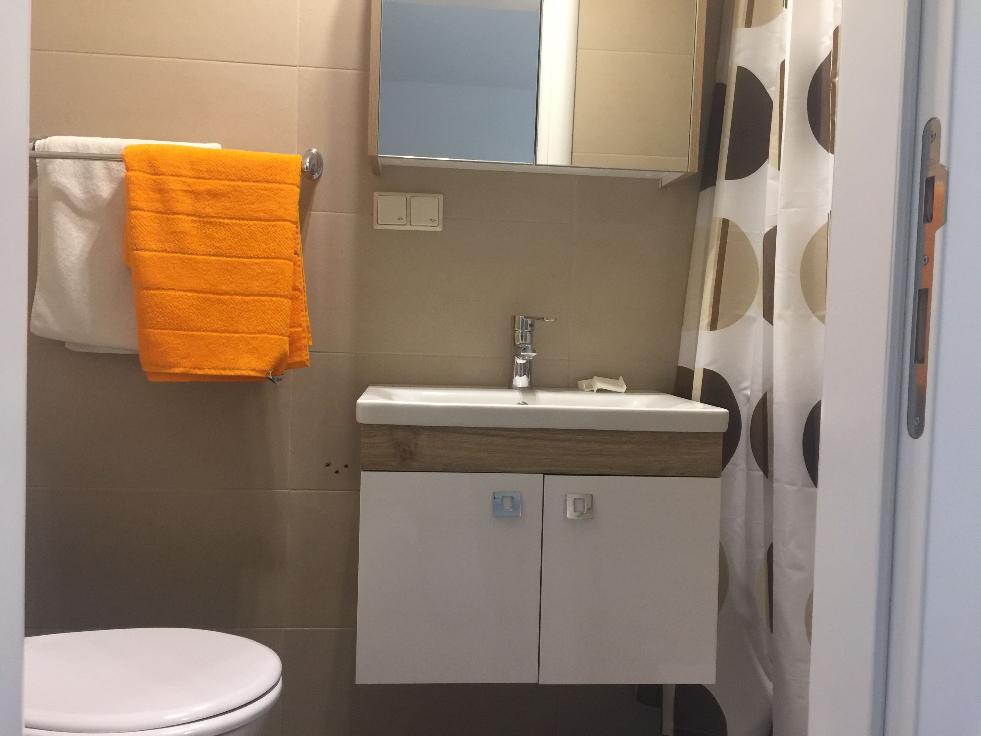 Kleines Badezimmer mit Waschbecken, Spiegel, Duschvorhang und Handtüchern.