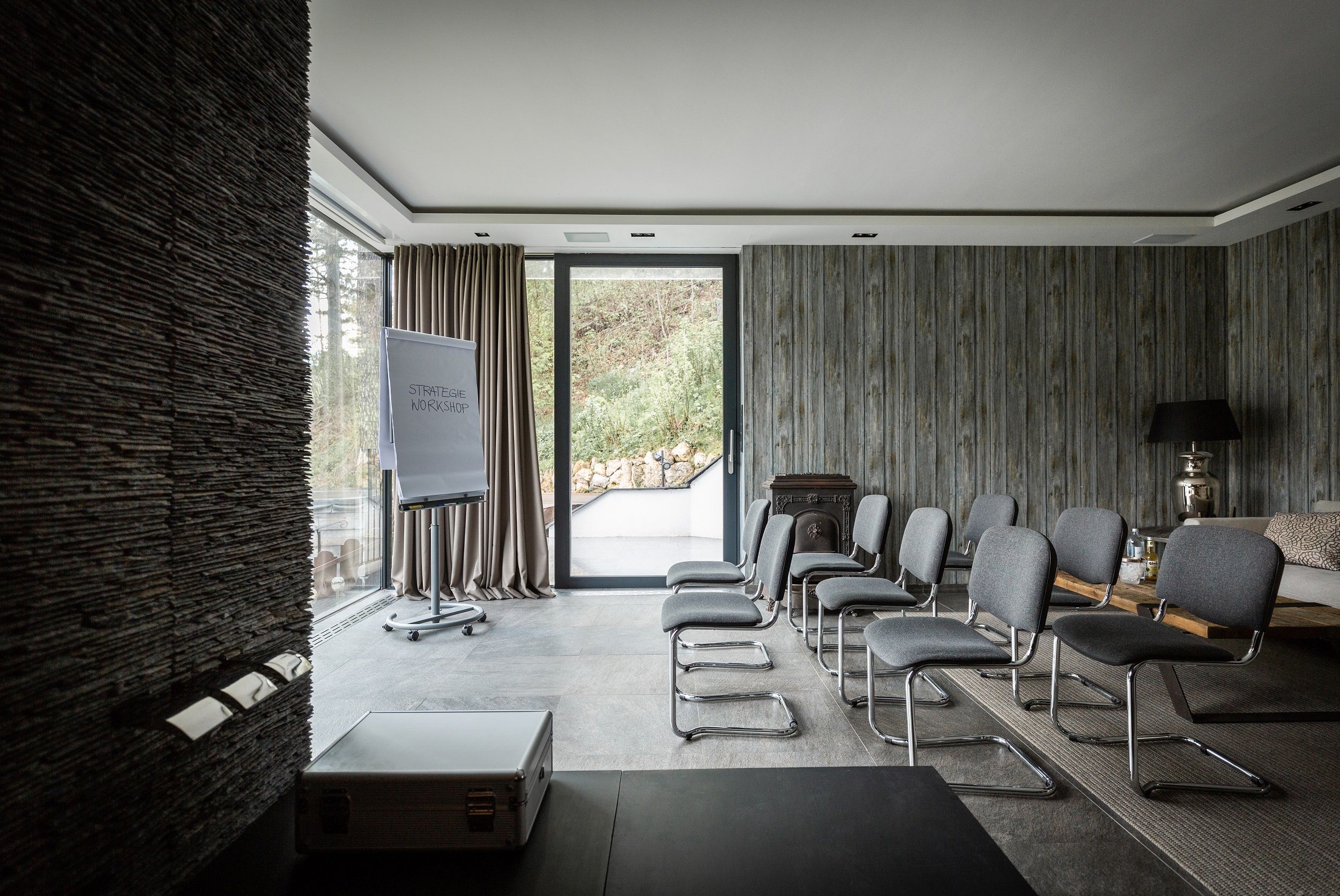 Moderner Konferenzraum mit grauen Stühlen, Flipchart und großen Fenstern.