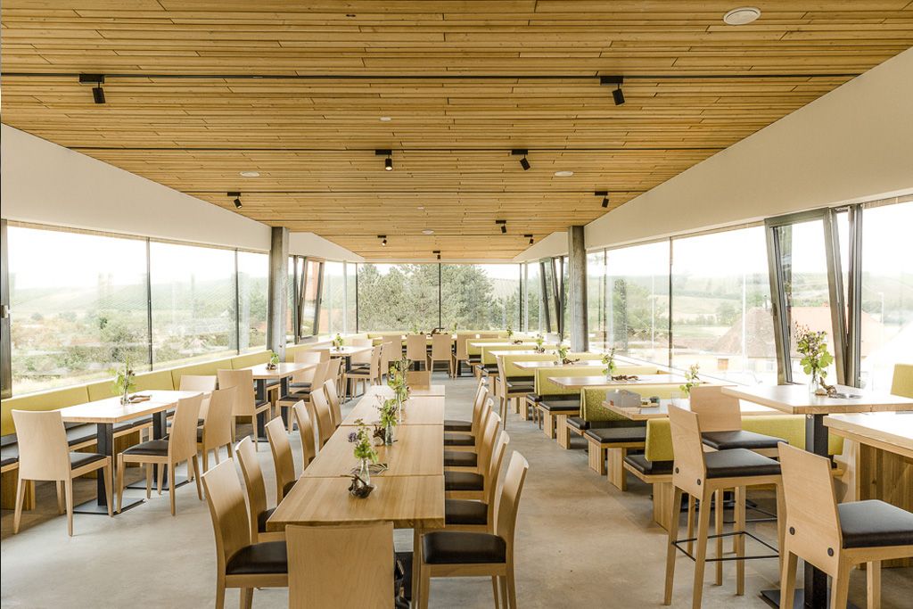 Innenansicht eines modernen Restaurants mit Holzmöbeln und großen Fenstern.