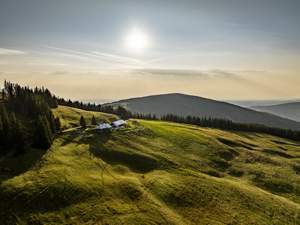 Landschaft mit grünen Hügeln, Wald und einem Gebäude unter der Sonne.