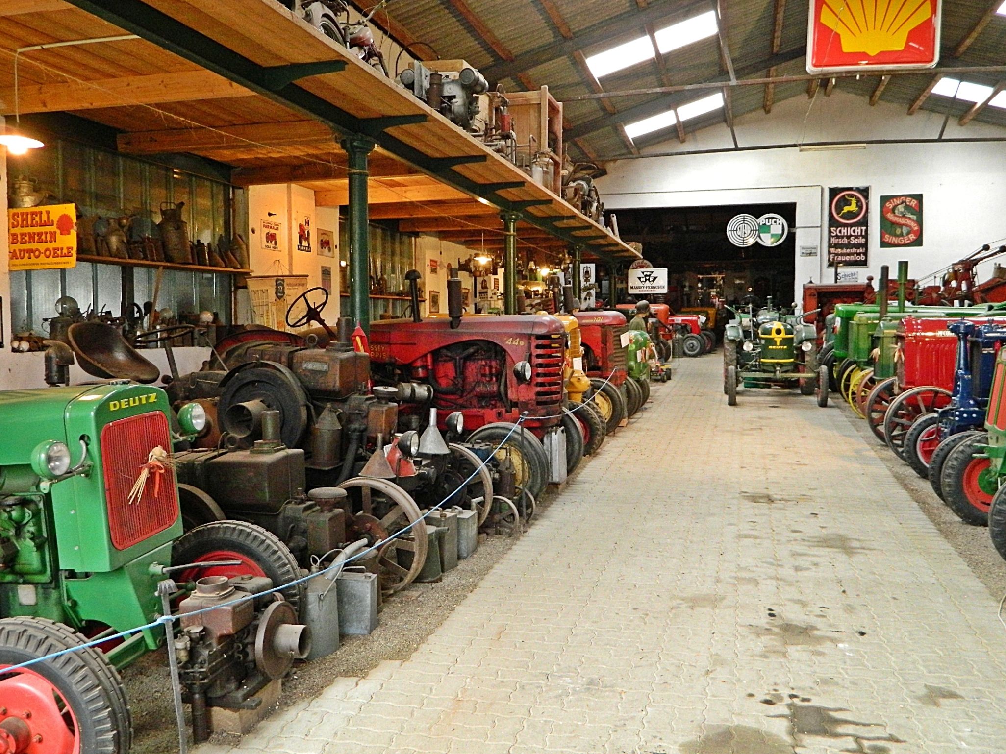 Innenansicht eines Traktorenmuseums mit alten Traktoren und Werbeschildern.
