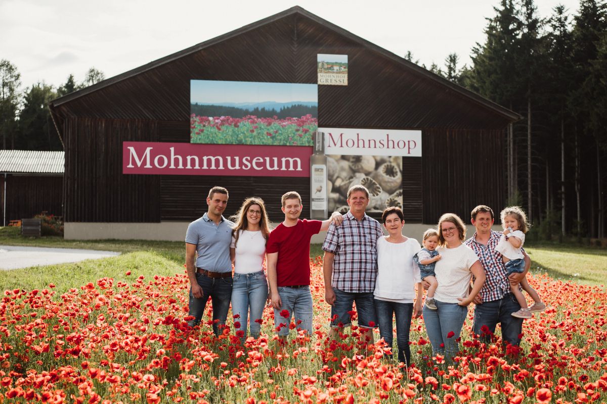 Eine Familie steht in einem Mohnfeld vor einem Gebäude mit der Aufschrift 'Mohnmuseum'.
