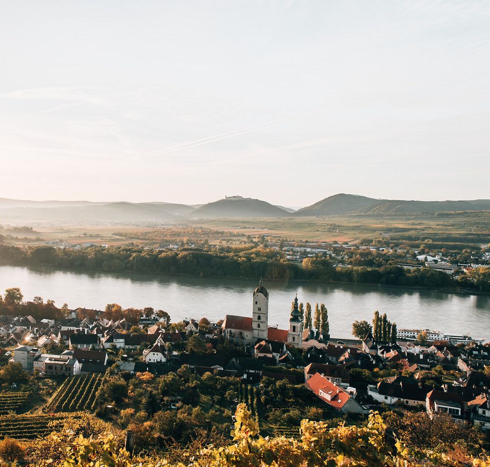 Die sanften Hügel und die glitzernde Donau schaffen eine malerische Kulisse, die zum Verweilen einlädt. Die Weinreben, die sich an den Hängen entlangziehen, versprechen genussvolle Erlebnisse und laden dazu ein, die regionale Weinkultur zu entdecken.