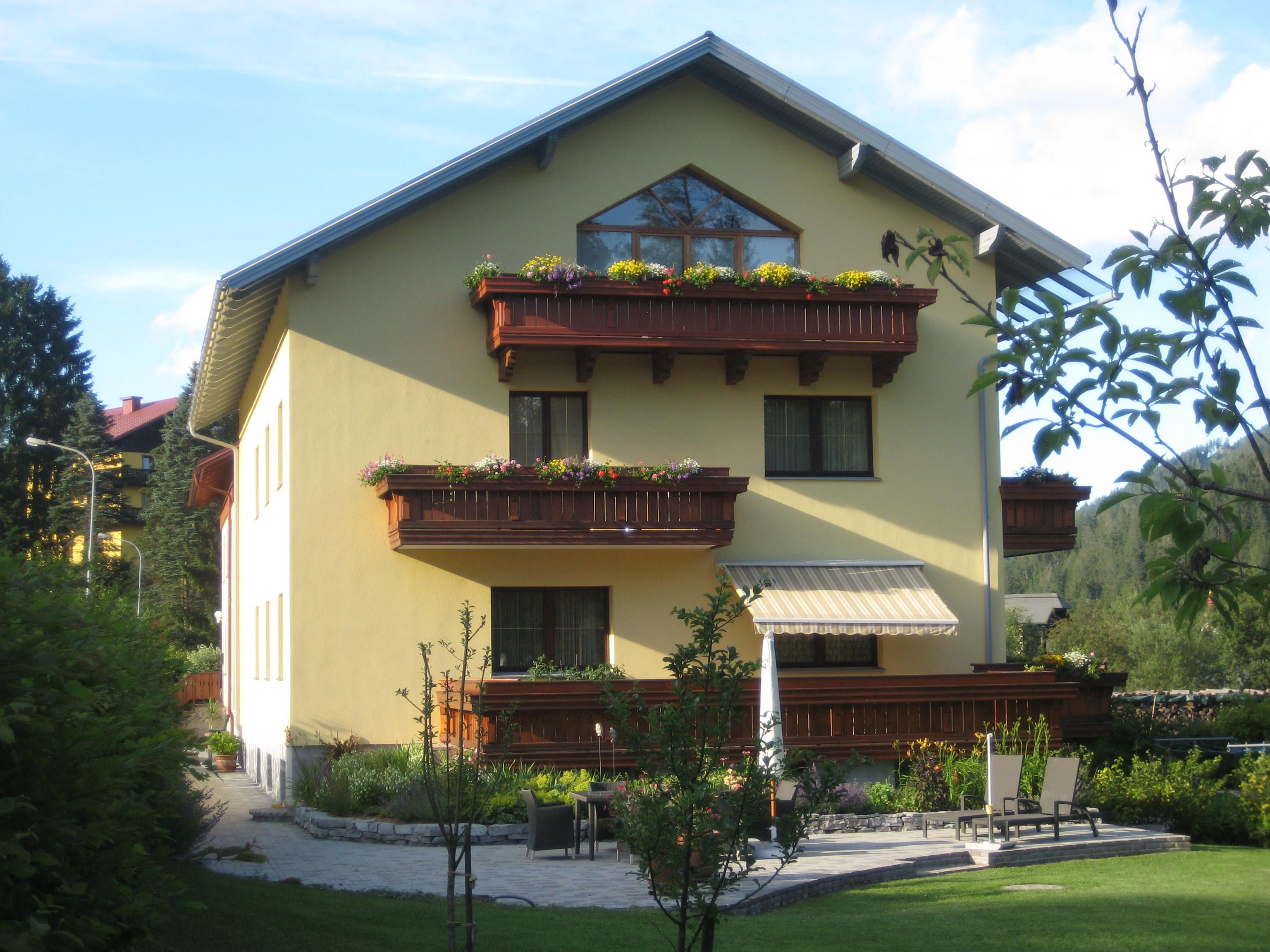 Gelbes Haus mit Holzbalkonen und Garten.