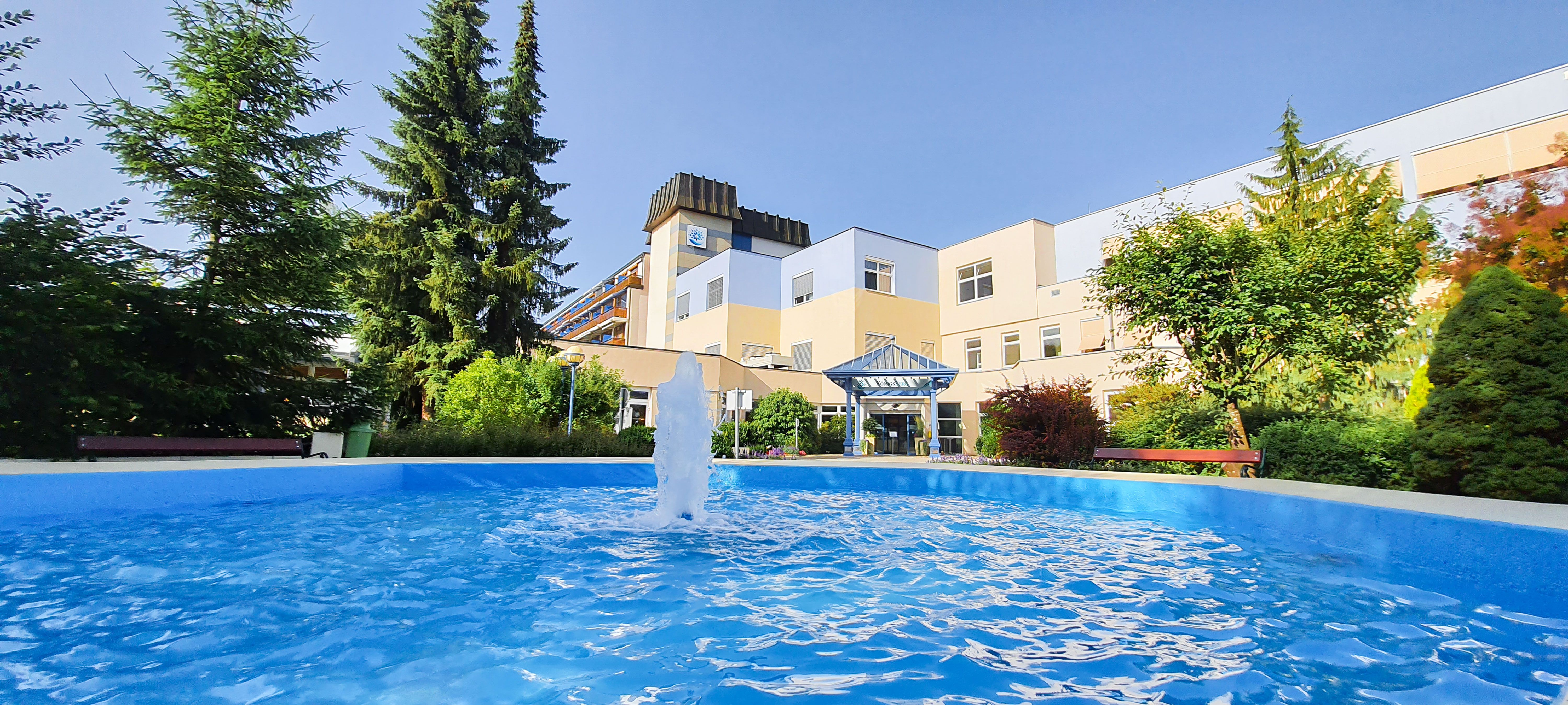 Außenansicht eines Gesundheitsresorts mit Springbrunnen und Garten.