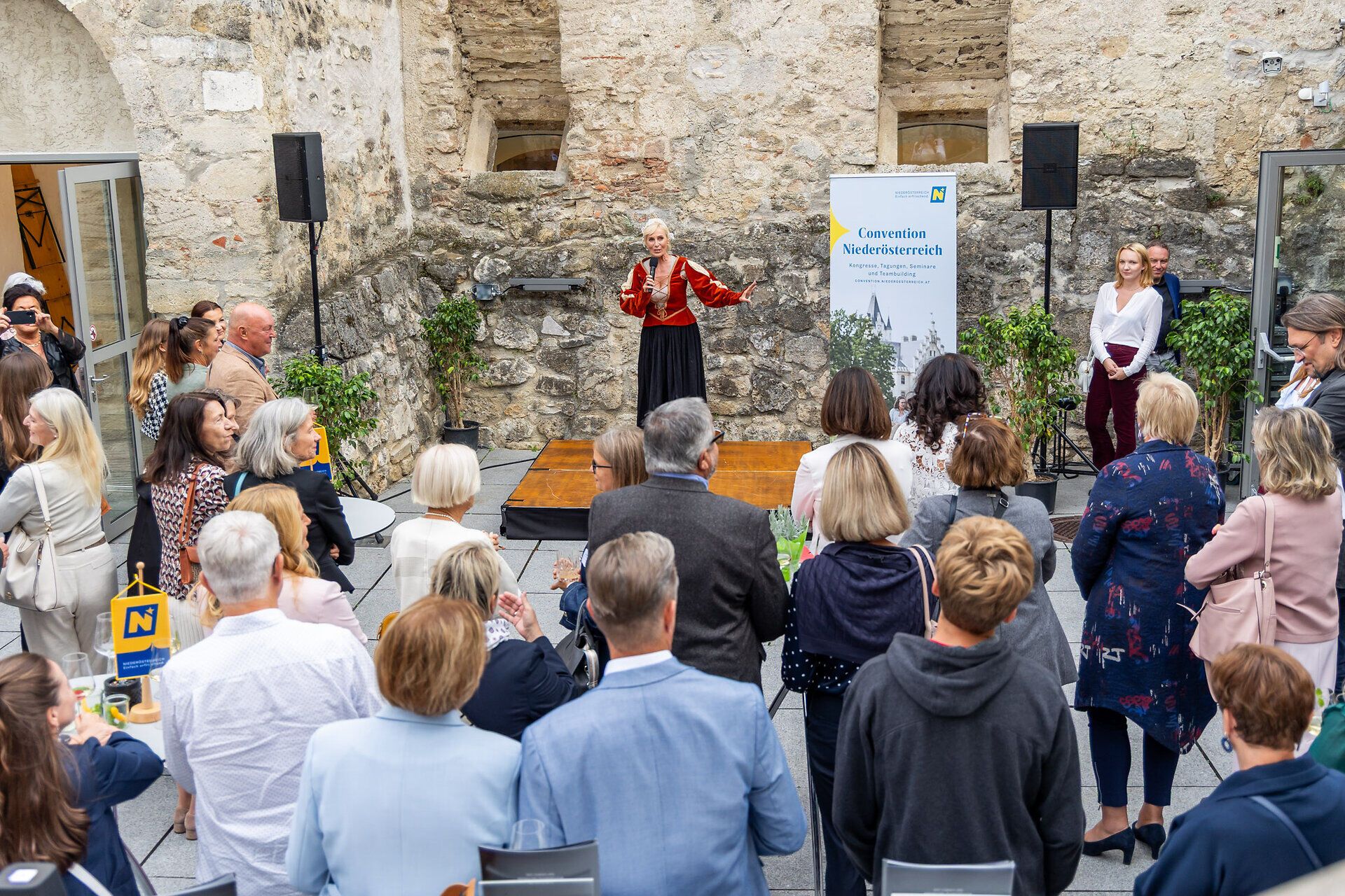 Eine Rednerin spricht beim Jubiläumsevent des Convention Bureau Niederösterreich in der Burg Perchtoldsdorf vor zahlreichen Gästen.