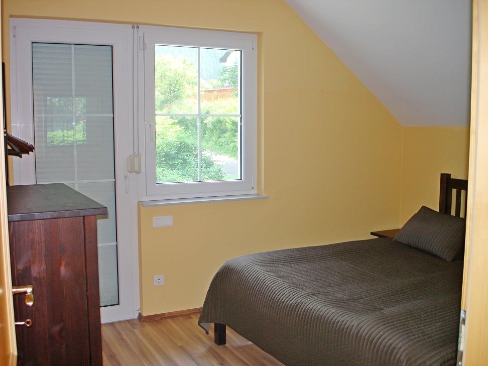 Ein kleines Schlafzimmer mit gelben Wänden, einem Einzelbett und einem Fenster mit Blick ins Grüne.