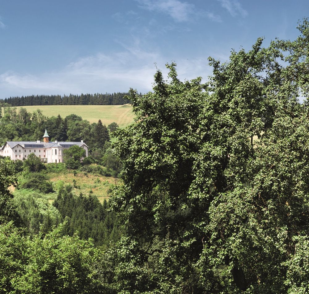 Ein Hotelgebäude inmitten einer grünen Landschaft mit Bäumen und Hügeln im Hintergrund.