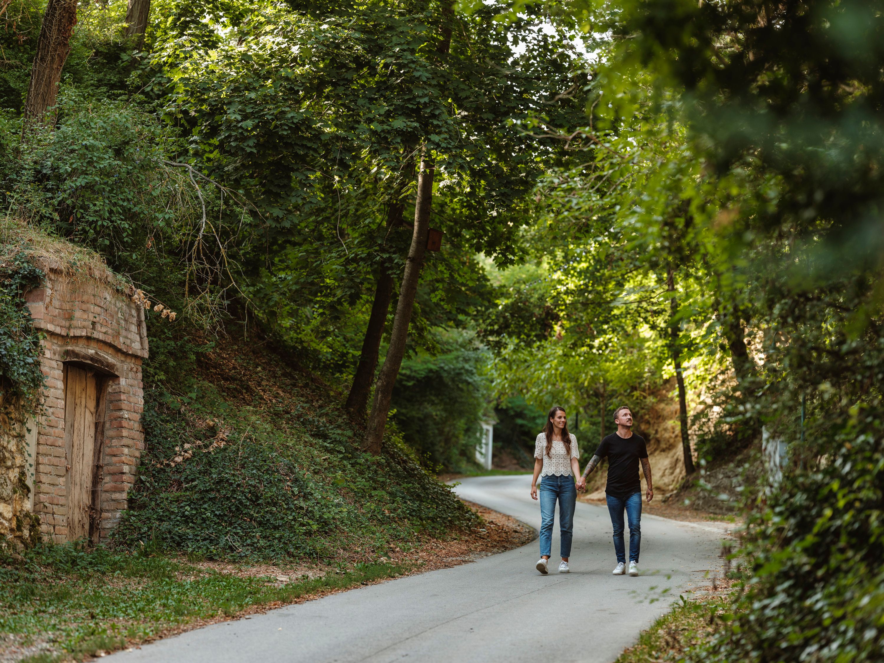 Ein Paar spaziert auf einer von Bäumen gesäumten Straße in einer ländlichen Umgebung.