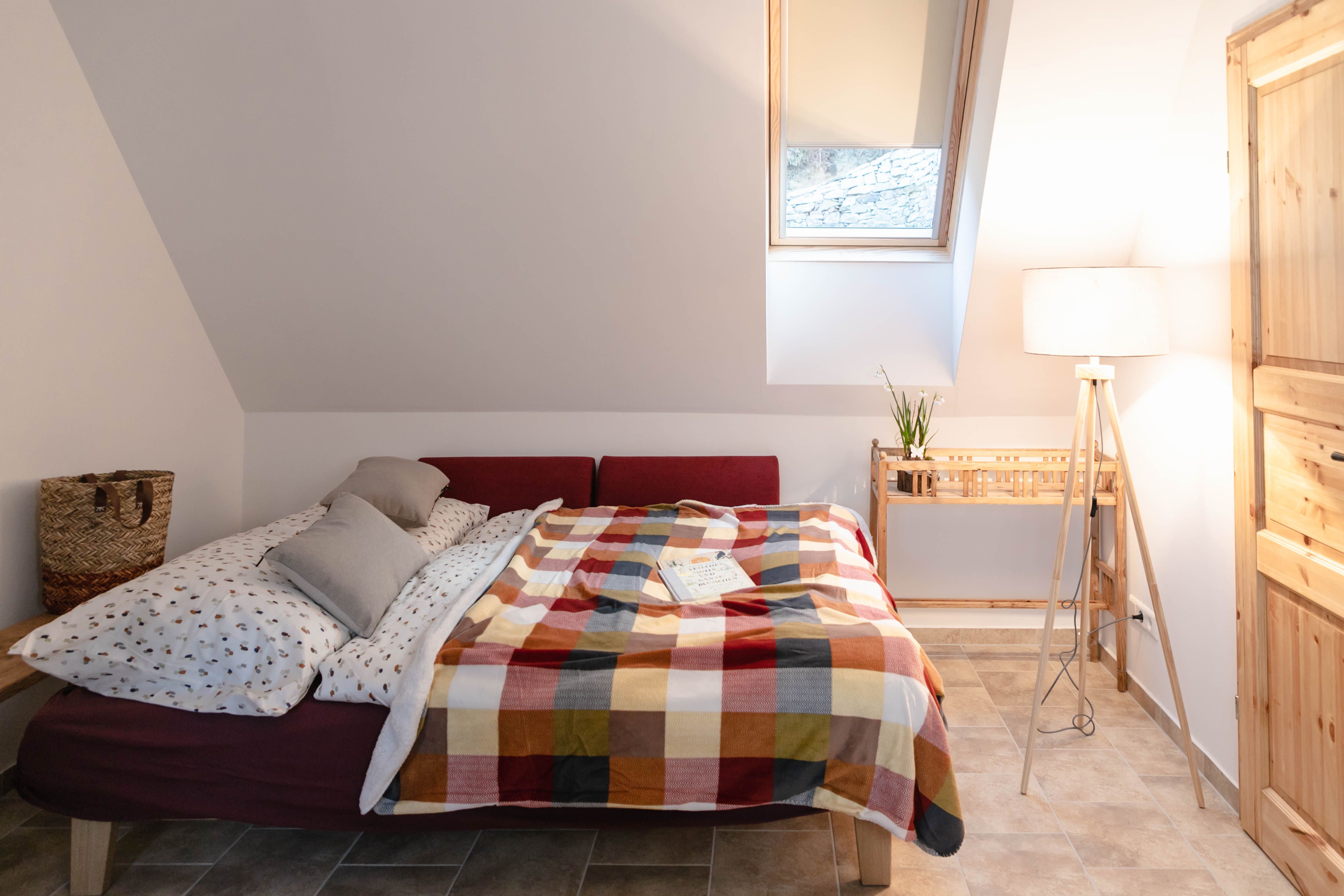 Gemütliches Schlafzimmer mit Bett, bunter Decke und Leselampe.