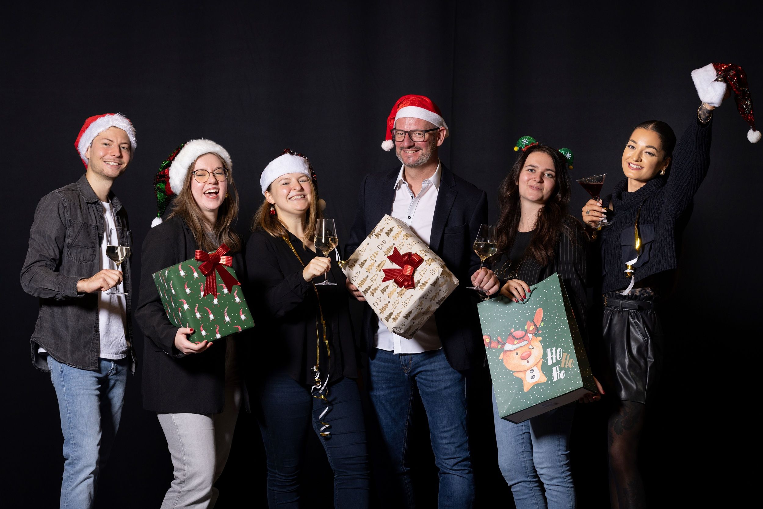 6 Personen in Weihnachtsmützen vor schwarzem Hintergrund