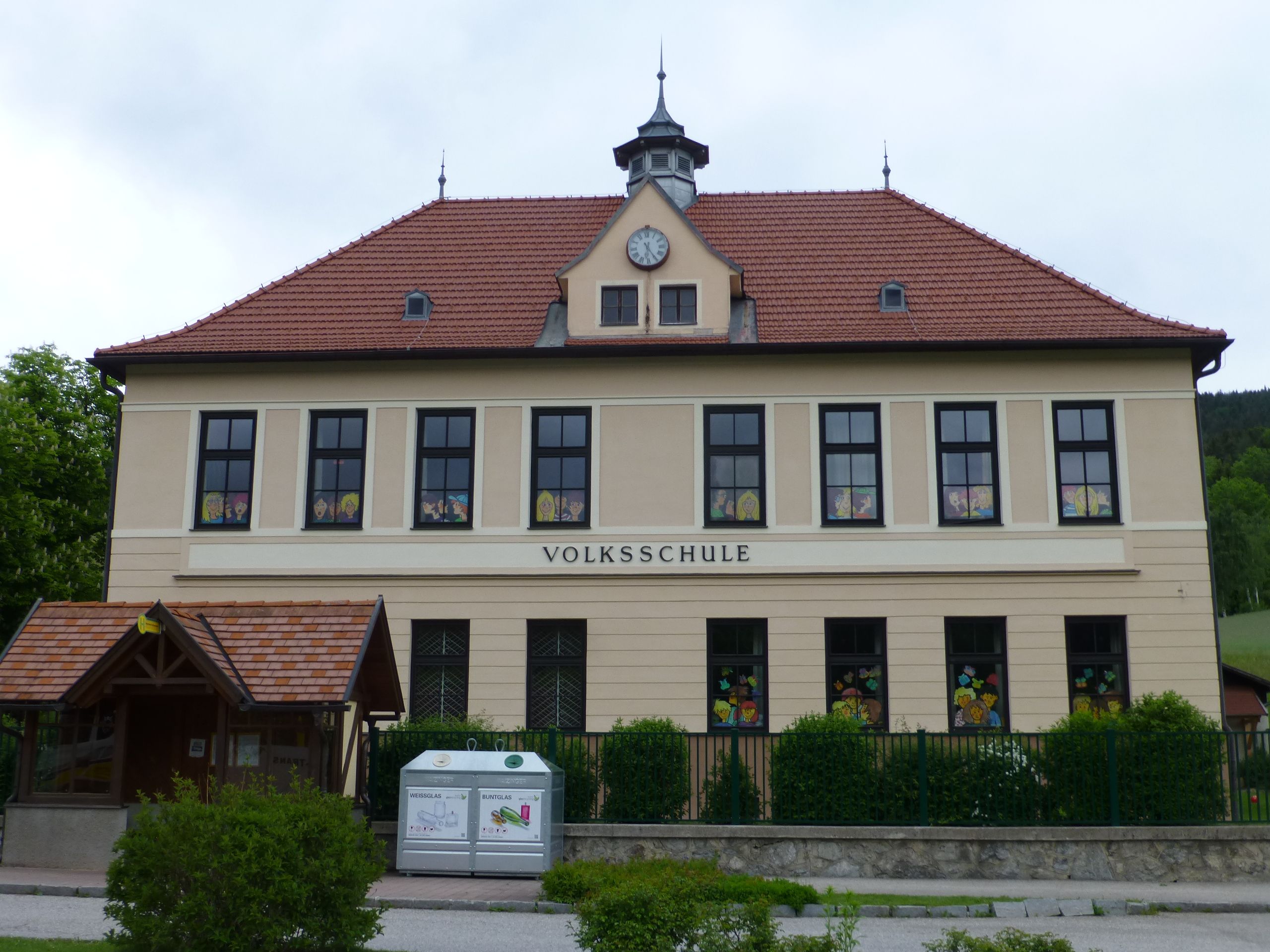 Vorderansicht der Volksschule Otterthal mit roten Dachziegeln und dekorierten Fenstern.
