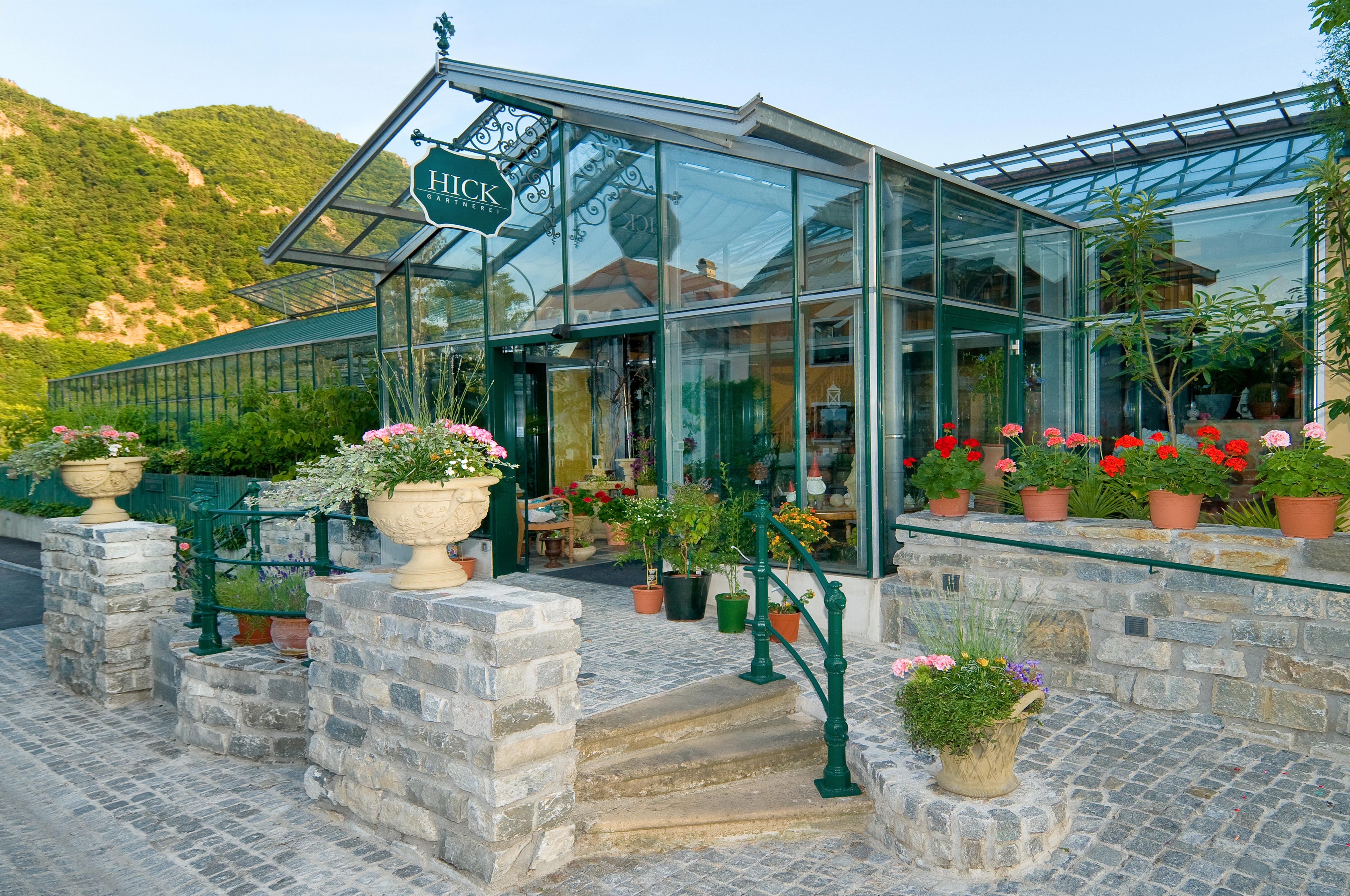 Eingang einer Gärtnerei mit Glasdach und Blumen in Töpfen.