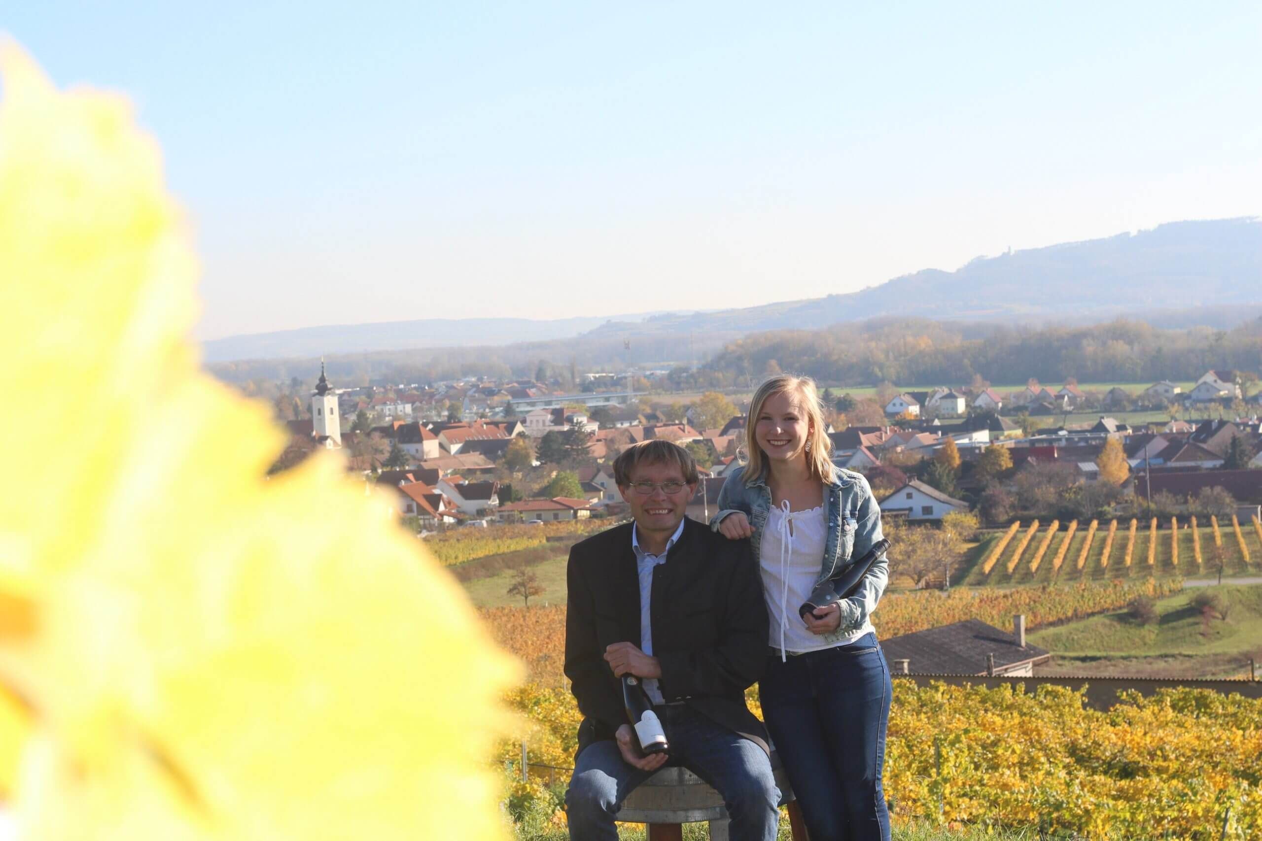 Zwei Personen in einem Weingarten mit Blick auf ein Dorf im Hintergrund.