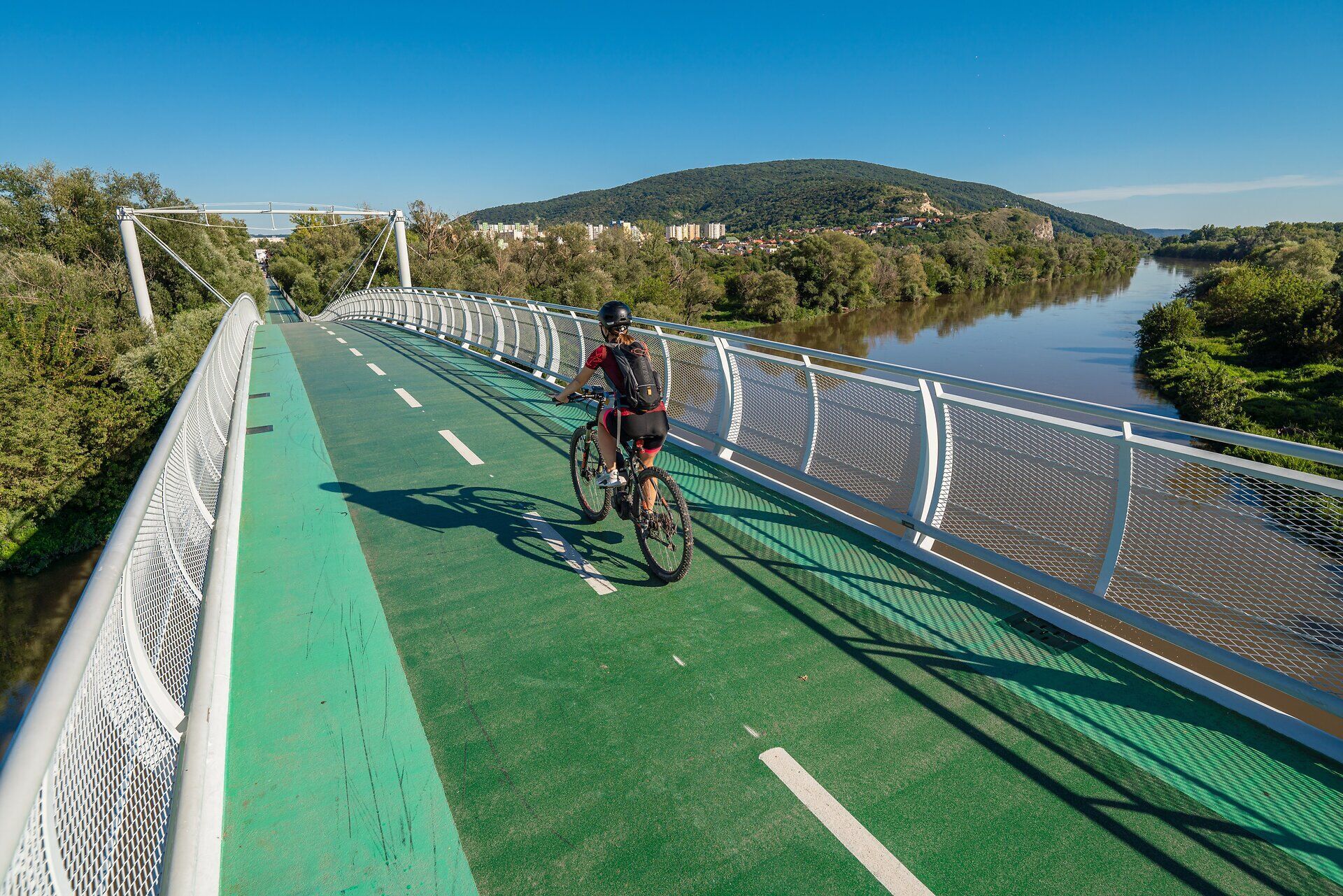 Die Brücke der Freiheit erstreckt sich majestätisch über den ruhigen Fluss, umgeben von üppigem Grün und sanften Hügeln. Radfahrer genießen die frische Luft und die atemberaubende Aussicht, während sie die Verbindung zwischen Natur und Kultur erleben. Ein perfekter Ort für einen unvergesslichen Ausblick und entspannte Stunden in der Natur.