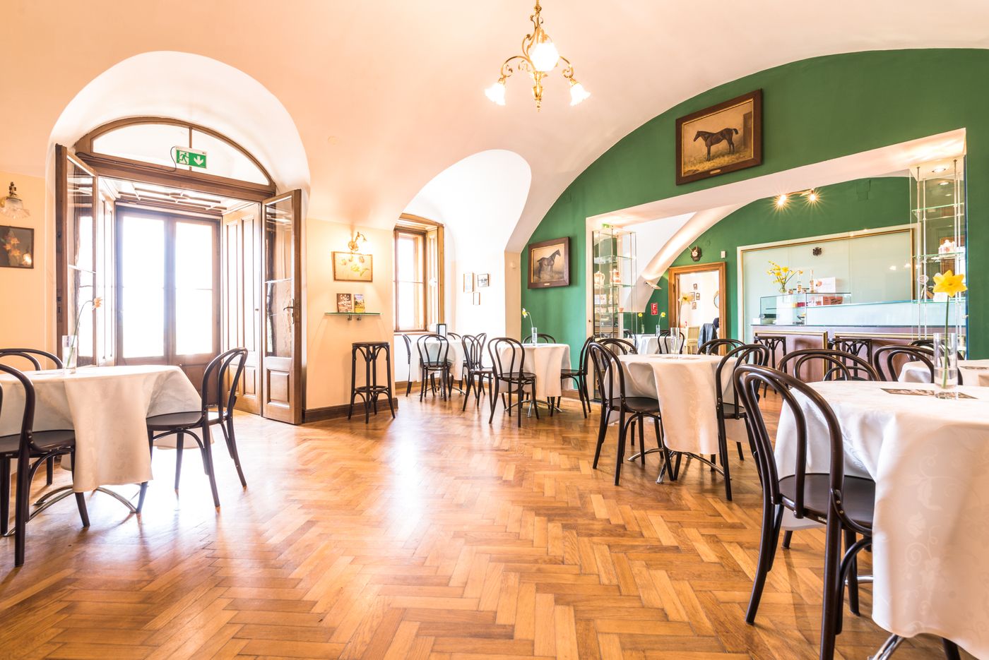 Innenansicht eines eleganten Cafés mit Holzboden, weißen Tischdecken und grüner Wand.