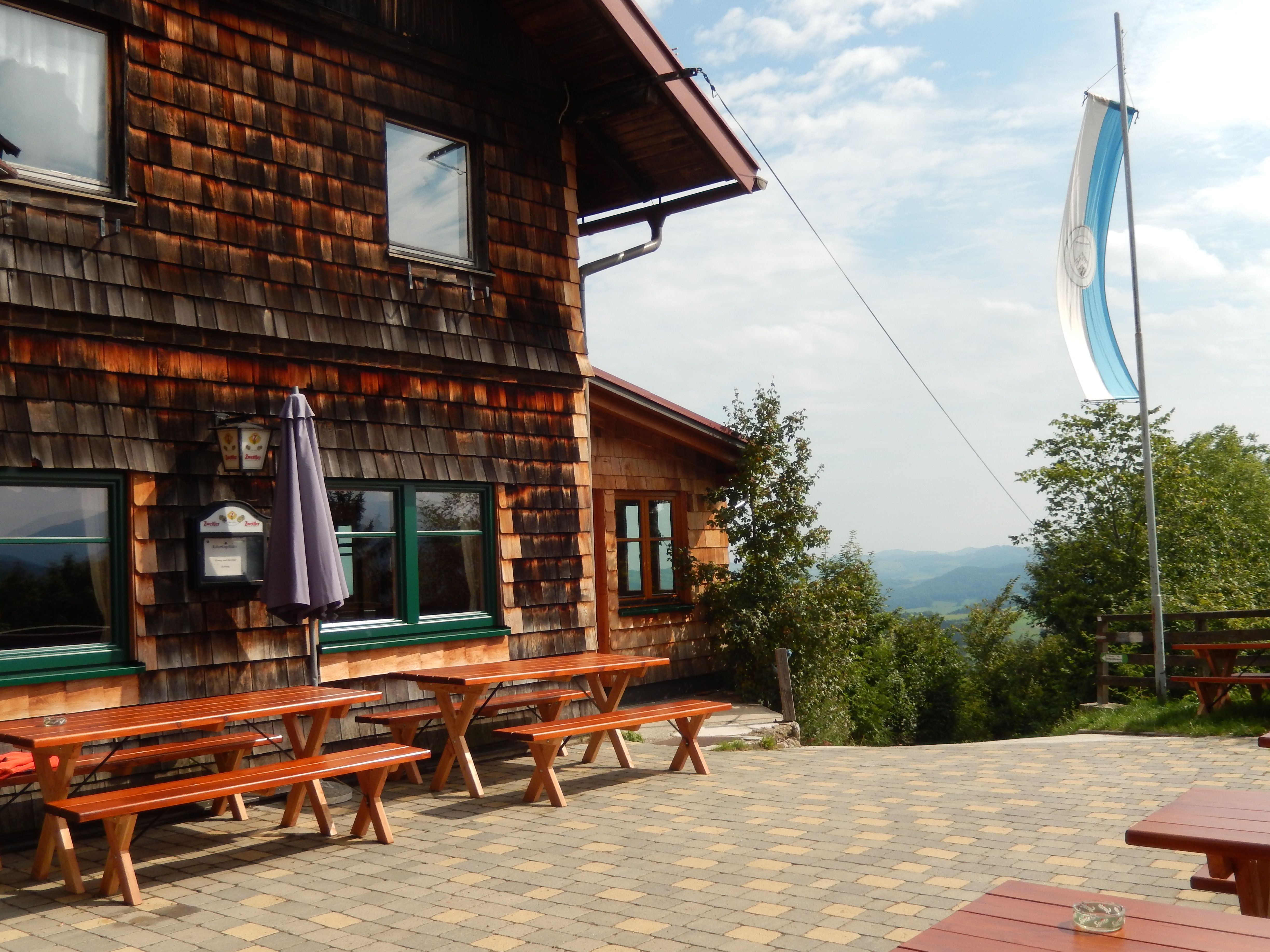 Holzhütte mit Terrasse und Bänken, Flagge weht im Wind.