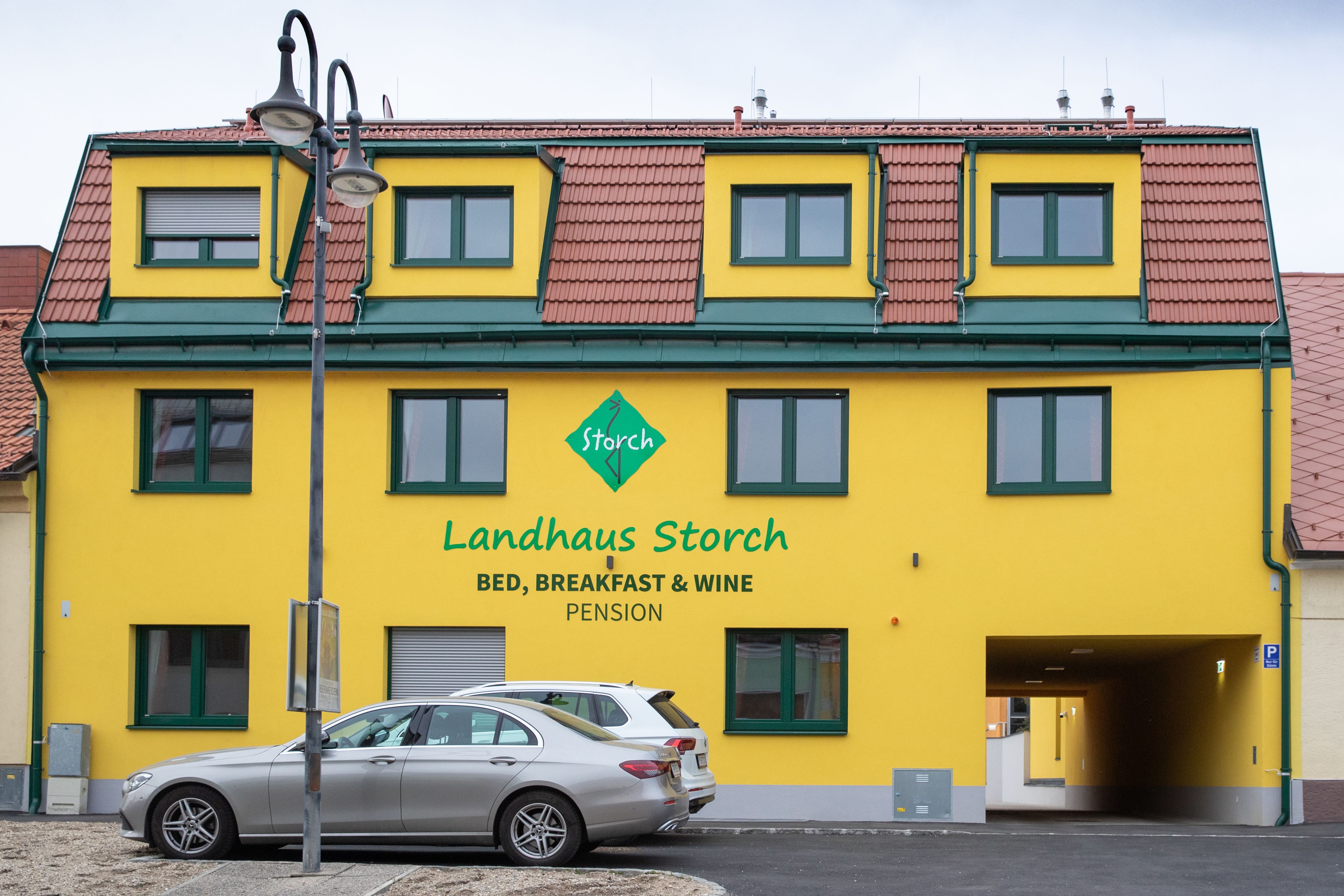 Gelbes Gebäude mit der Aufschrift 'Landhaus Storch', davor geparkte Autos.
