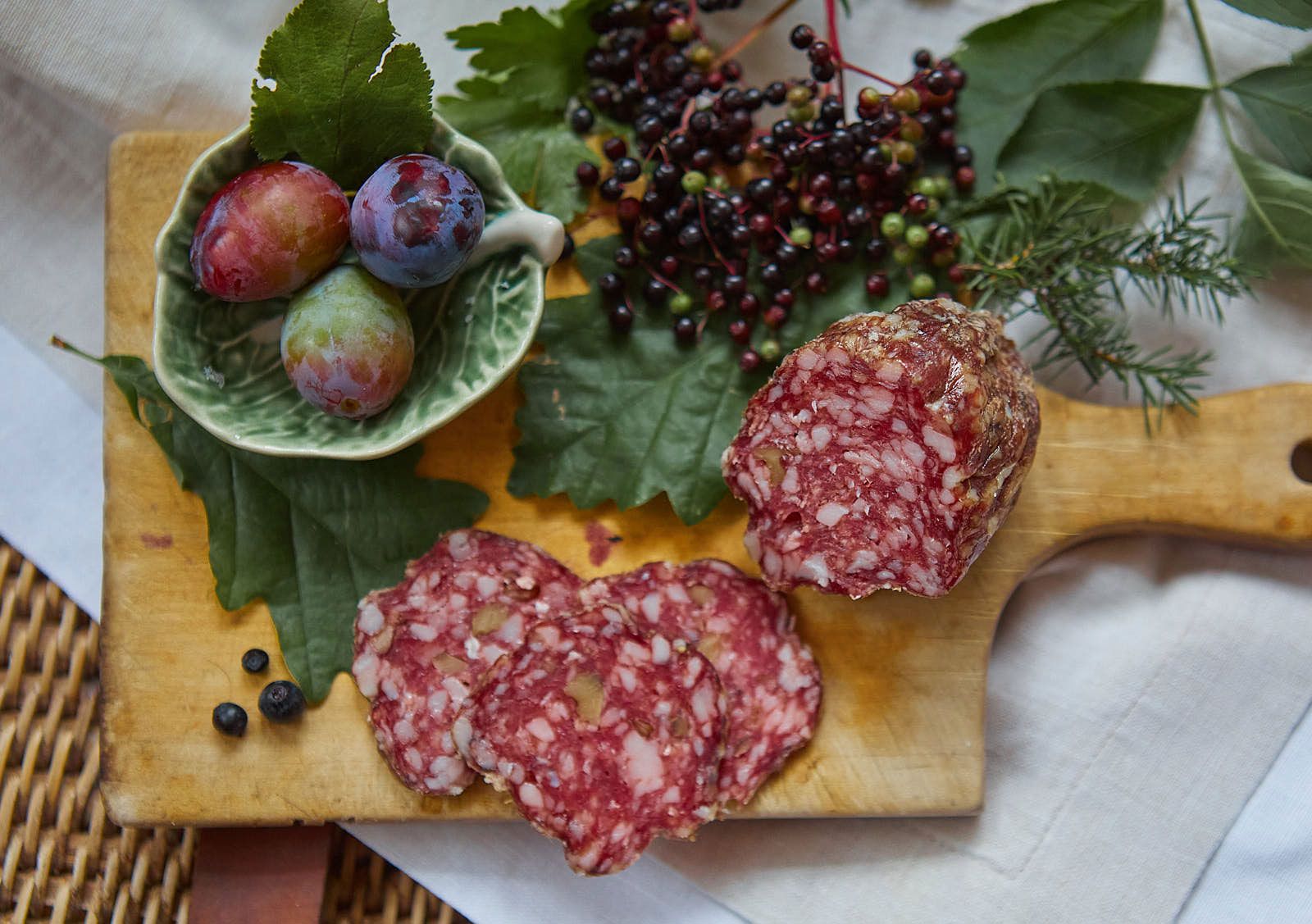 Nahaufnahme einer Salami auf einem Holzbrett mit Beeren und Pflaumen.