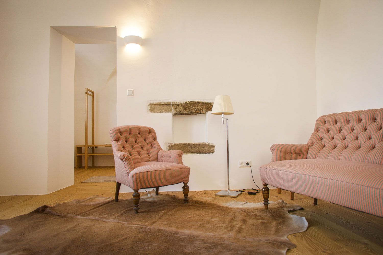 Ein gemütliches Wohnzimmer mit einem Sessel, einem Sofa, einer Stehlampe und einem Teppich auf Holzboden.