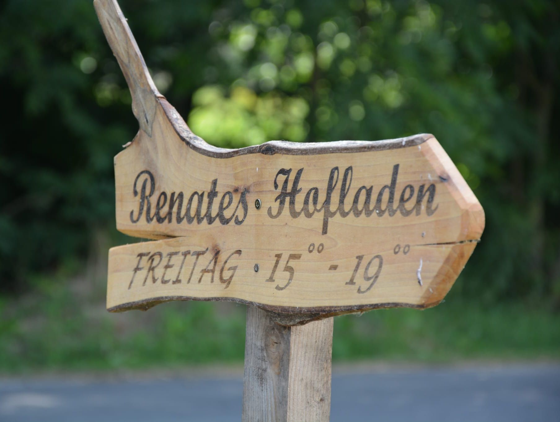 Holzschild mit der Aufschrift 'Renates Hofladen' und Öffnungszeiten 'Freitag 15-19 Uhr'.