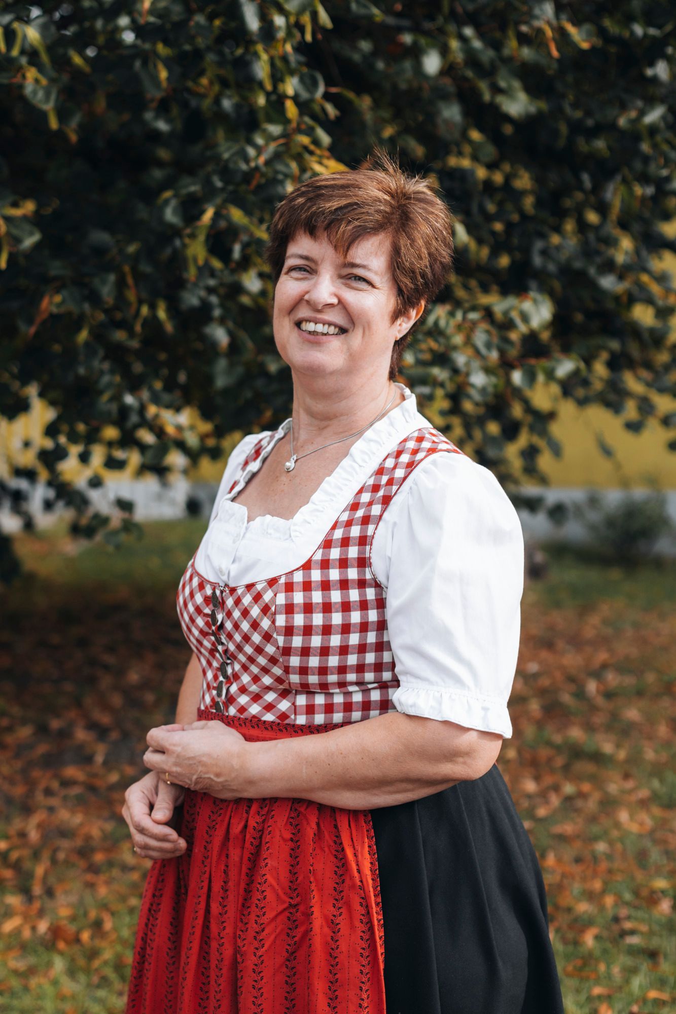 Frau in traditioneller Tracht vor einem Baum im Freien.