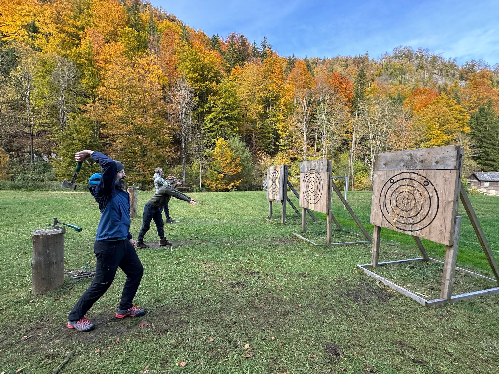 Personen werfen Äxte auf Zielscheiben im Freien, umgeben von herbstlichen Bäumen.
