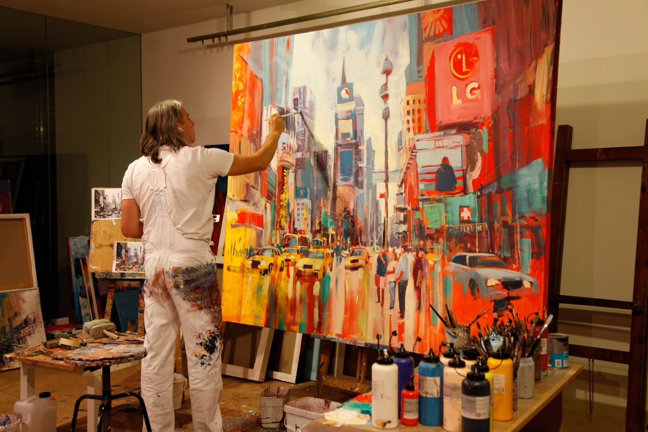 Ein Künstler malt ein lebhaftes Stadtbild auf einer großen Leinwand in einem Atelier.