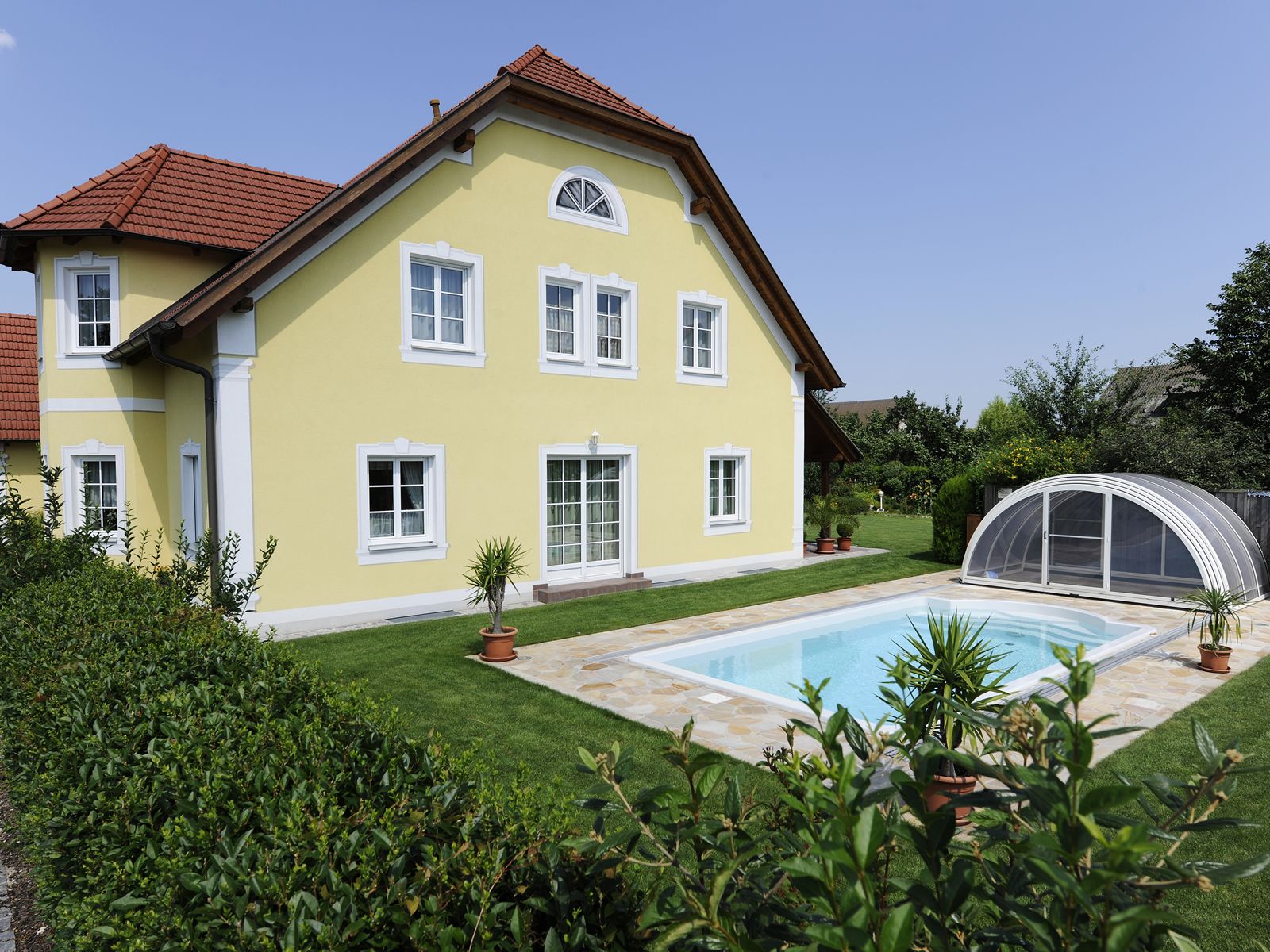 Gelbes Gästehaus mit rotem Dach und Pool im Garten.