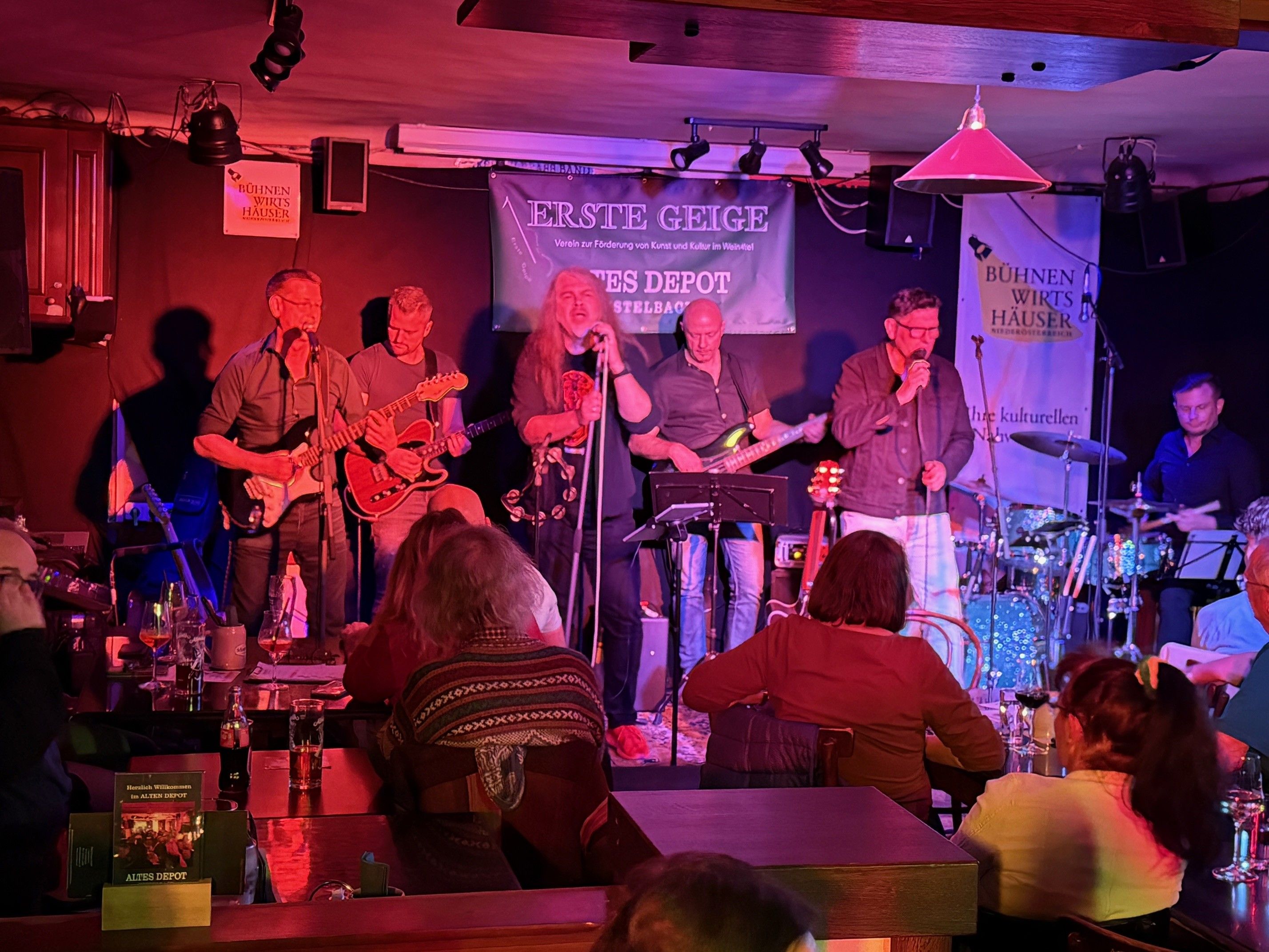 Band spielt auf einer Bühne in einem kleinen Veranstaltungsort mit Publikum.
