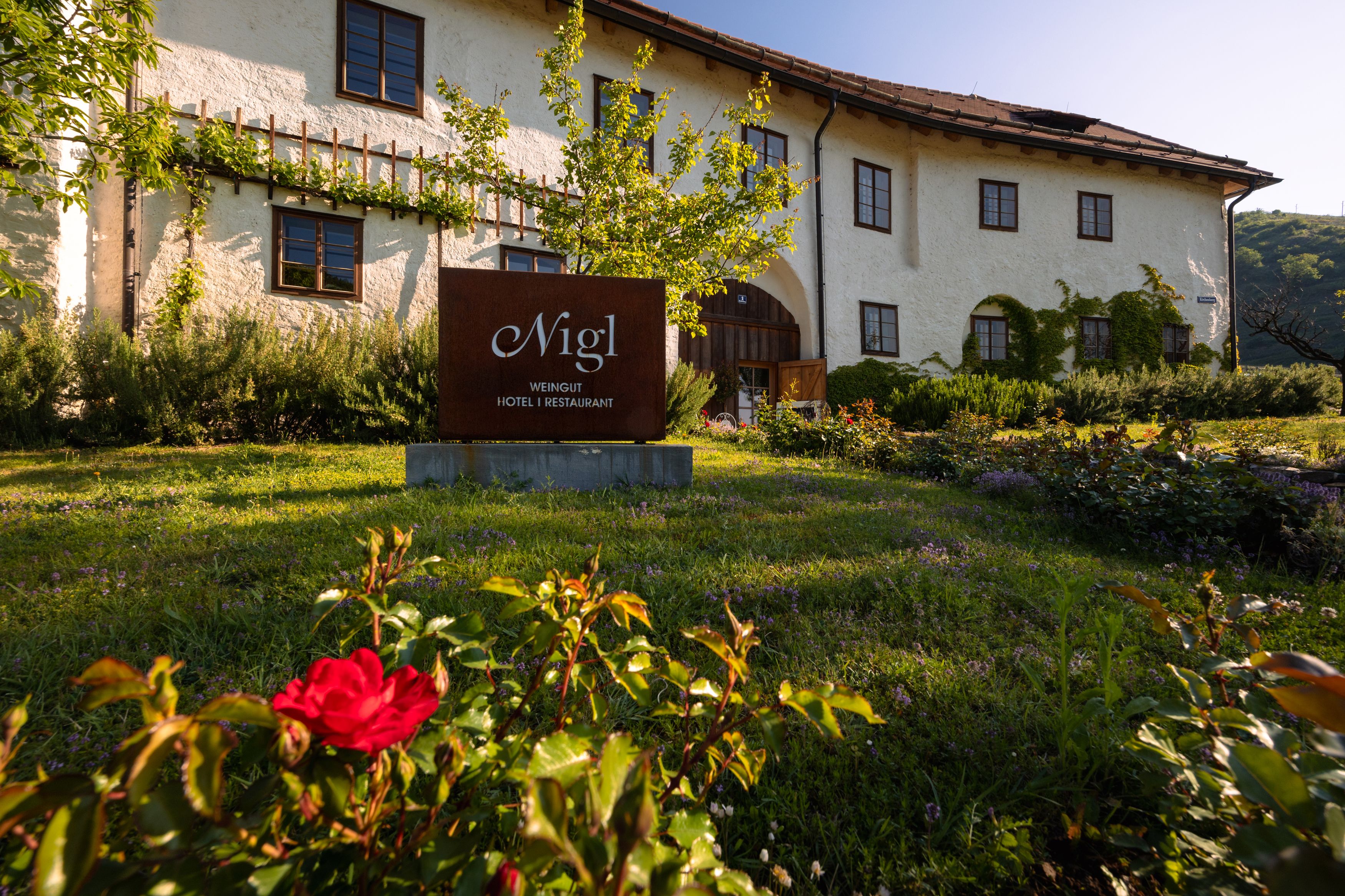 Außenansicht des Weinhotels Nigl mit Garten und Schild.