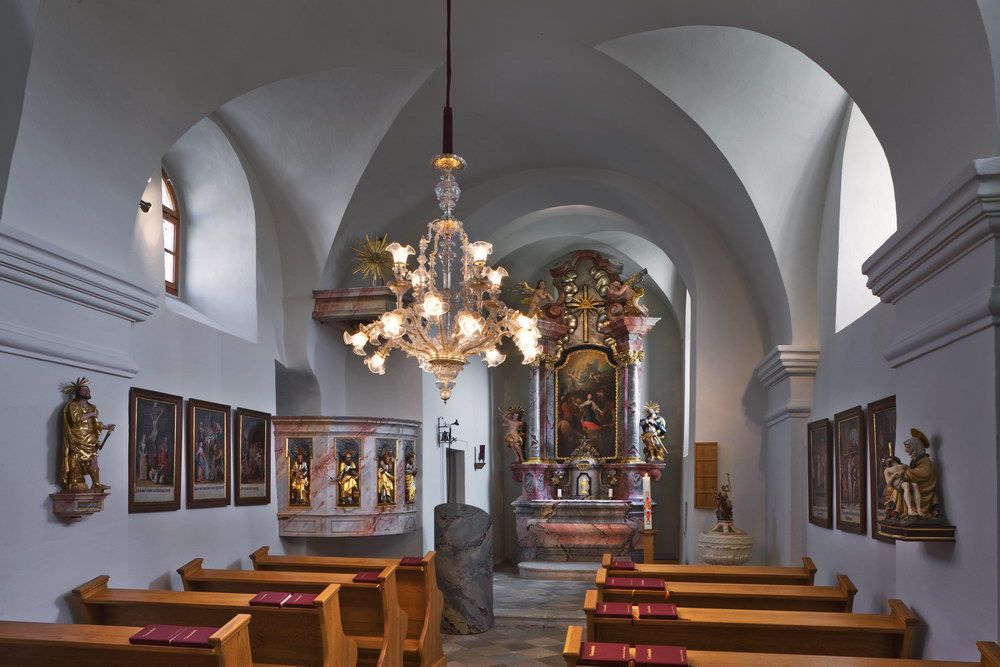 Innenansicht einer barocken Kirche mit Altar, Gemälden und einem Kronleuchter.