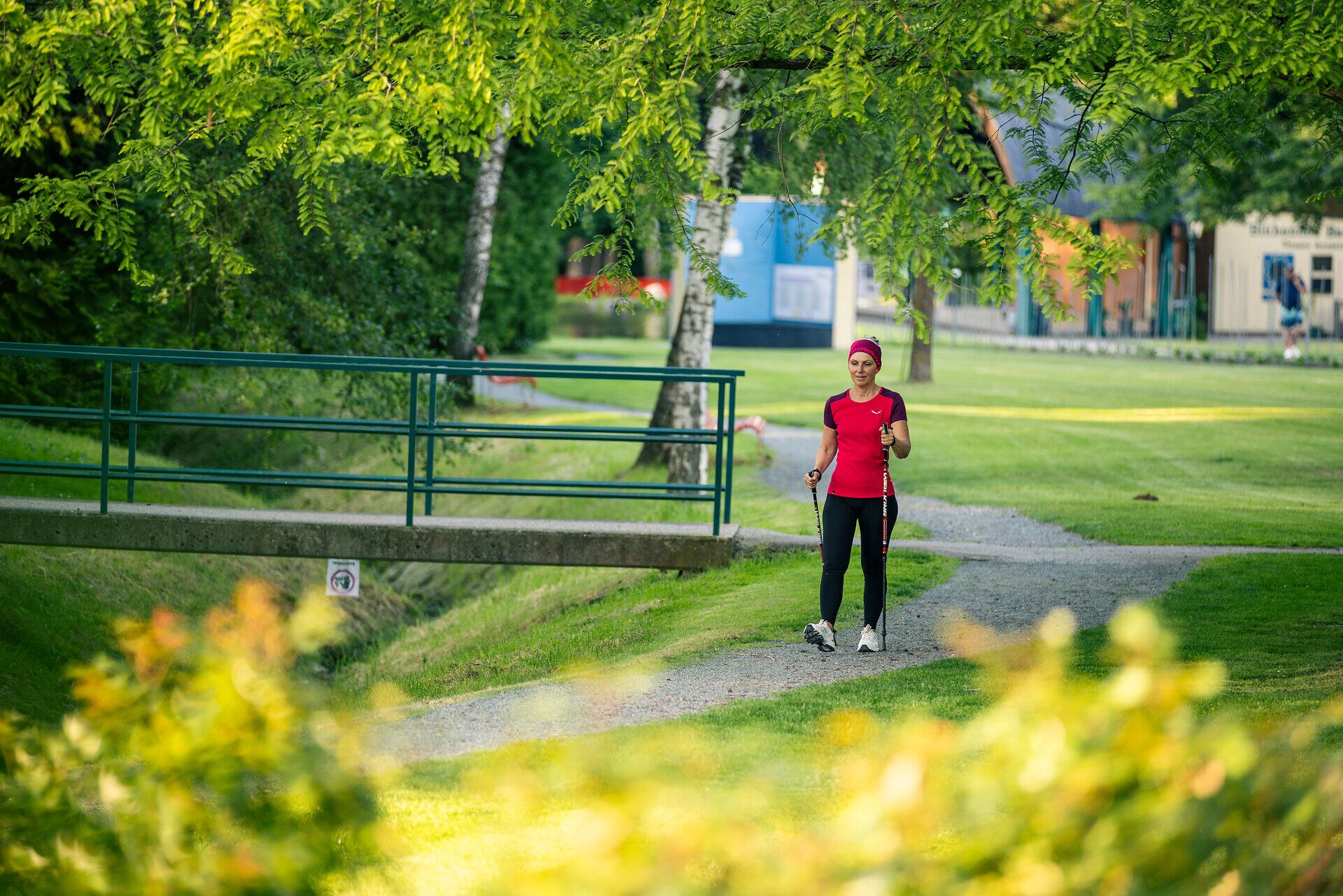 Eine sportlich gekleidete Frau geht mit Walkingstöcken durch den Kurpark Bad Schönau.