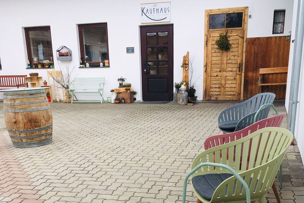 Sitzbereich vor einem Kaufhaus mit bunten Stühlen und einem Fass.